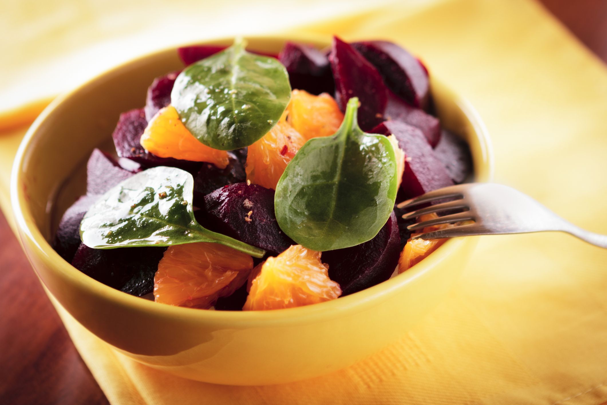 beet, oranges and spinach salad with ground pepper in yellow bowl macro
