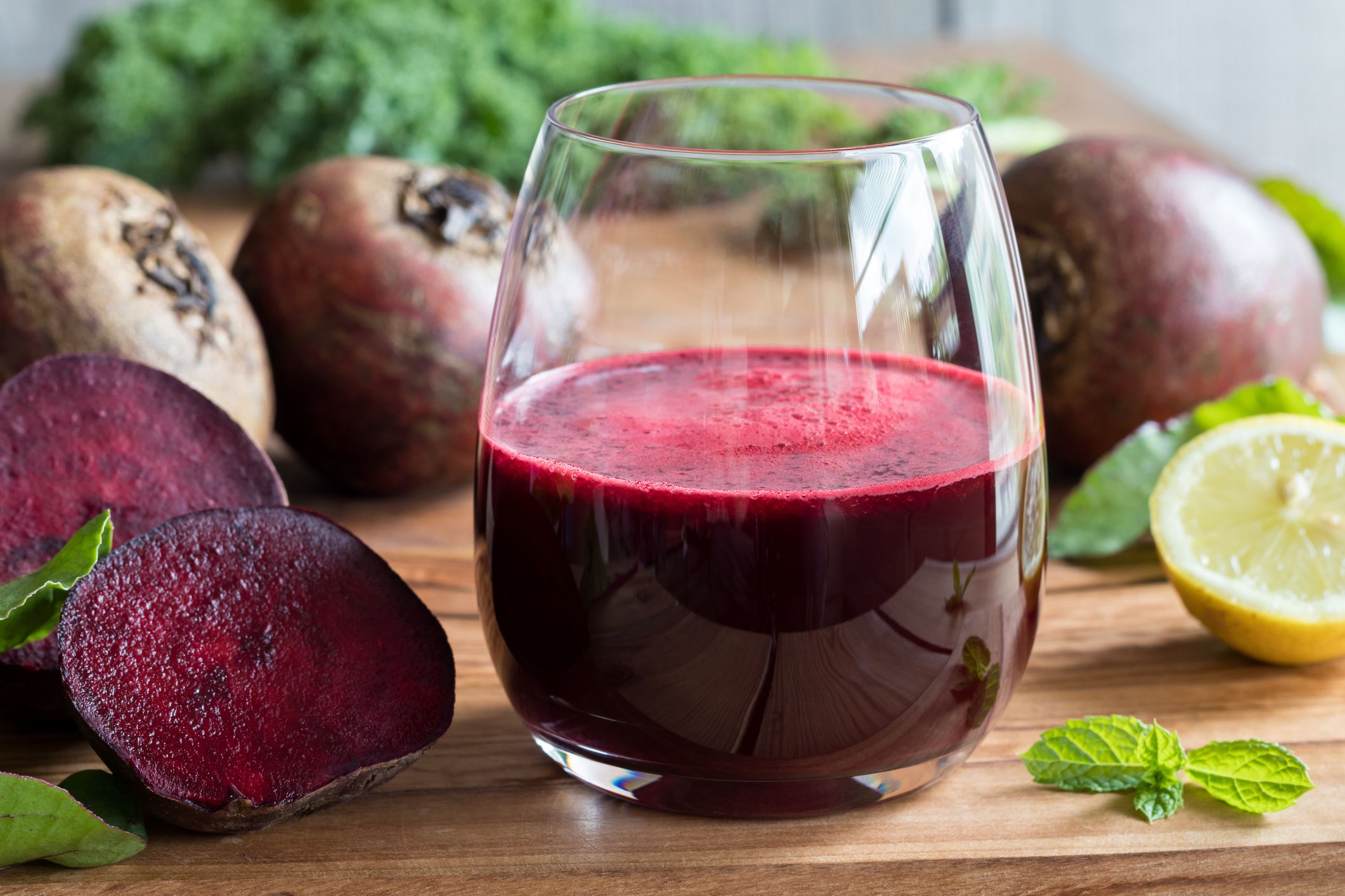 Red beet juice in a glass on a wooden background with lemon, beets and greens