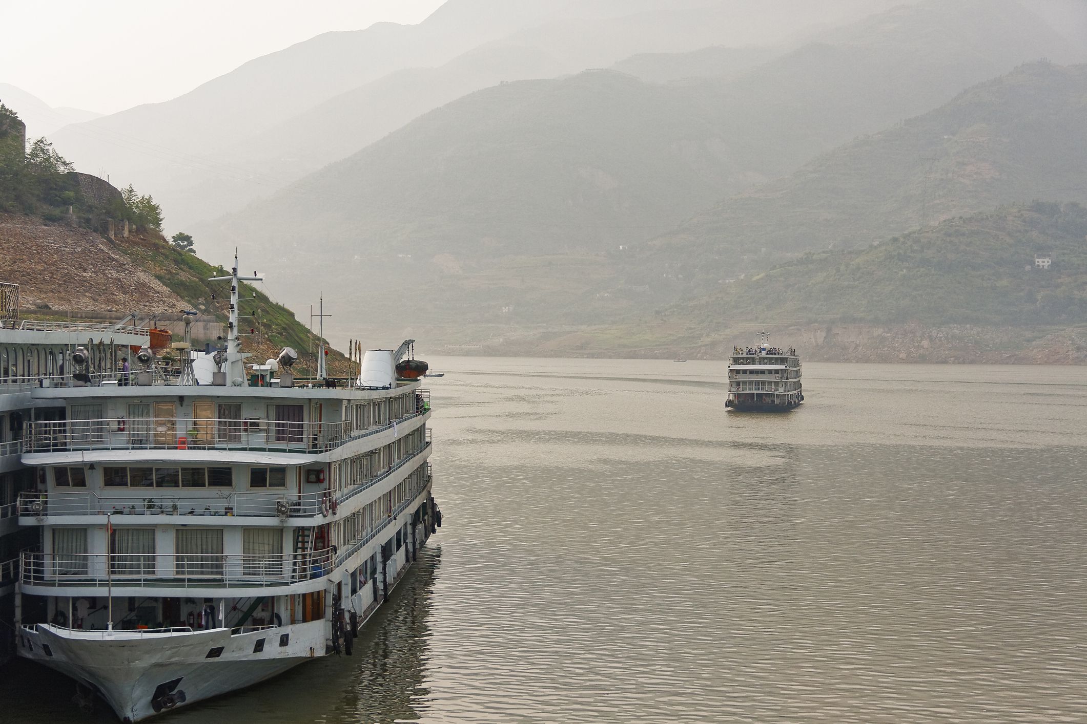 River cruise ship sailing on a hazy morning, other cruise ships are moored.
