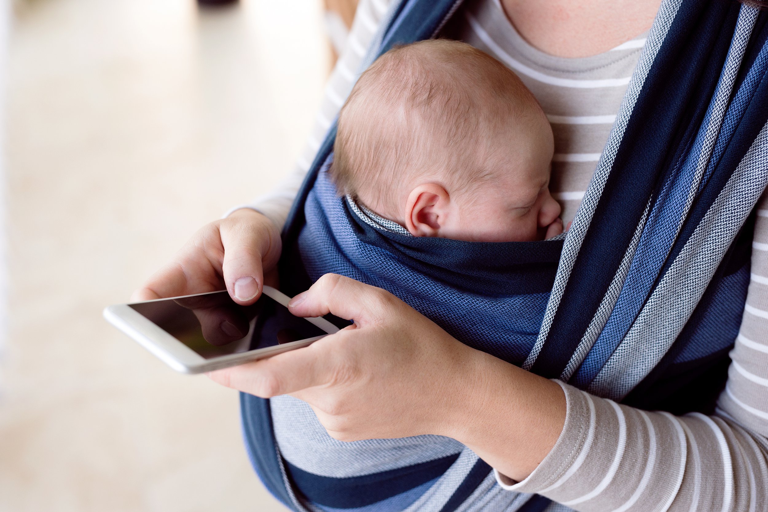 Woman holding her baby in a wrap while using her smartphone