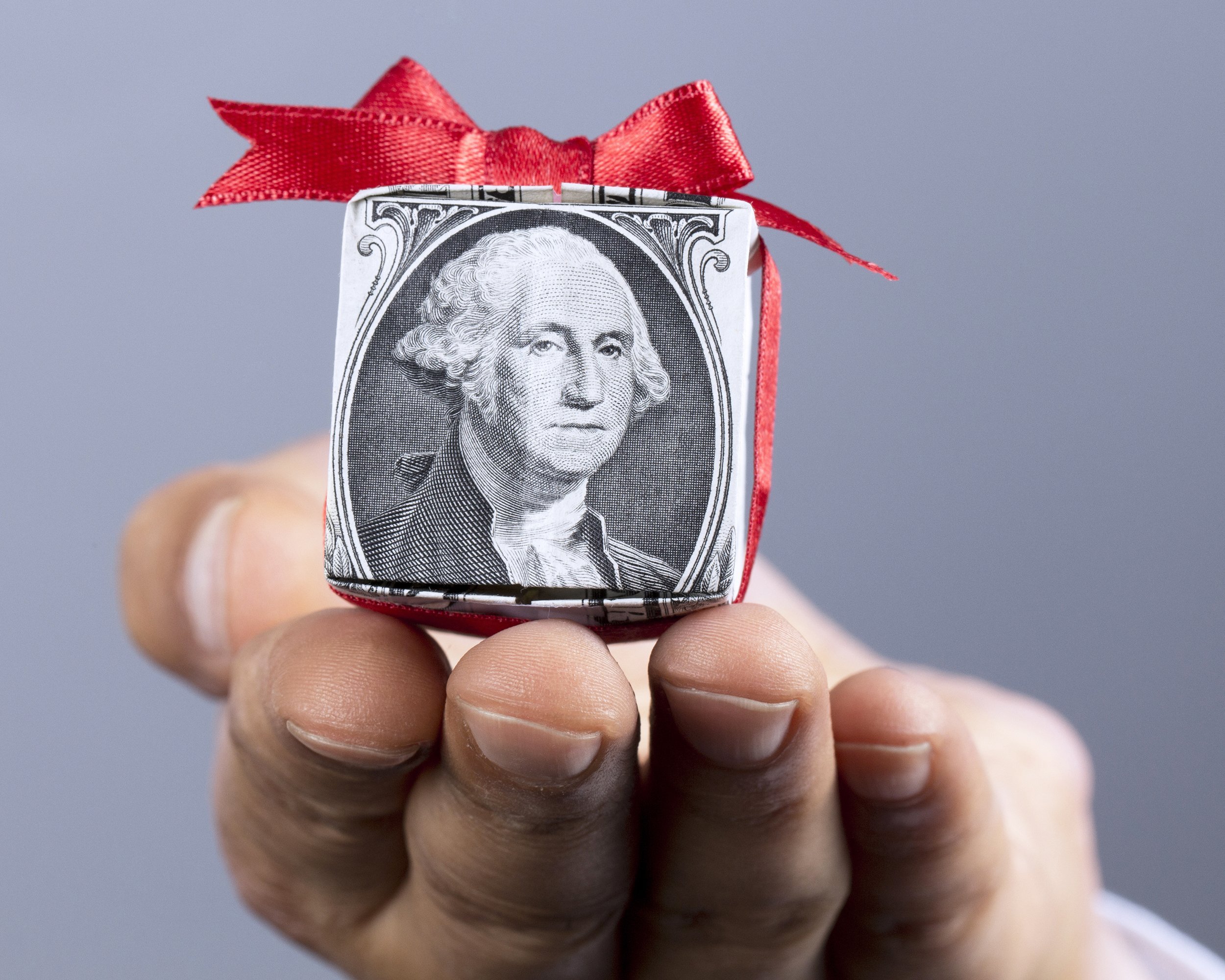 hand holding box made of a dollar bill with red ribbon bow on top