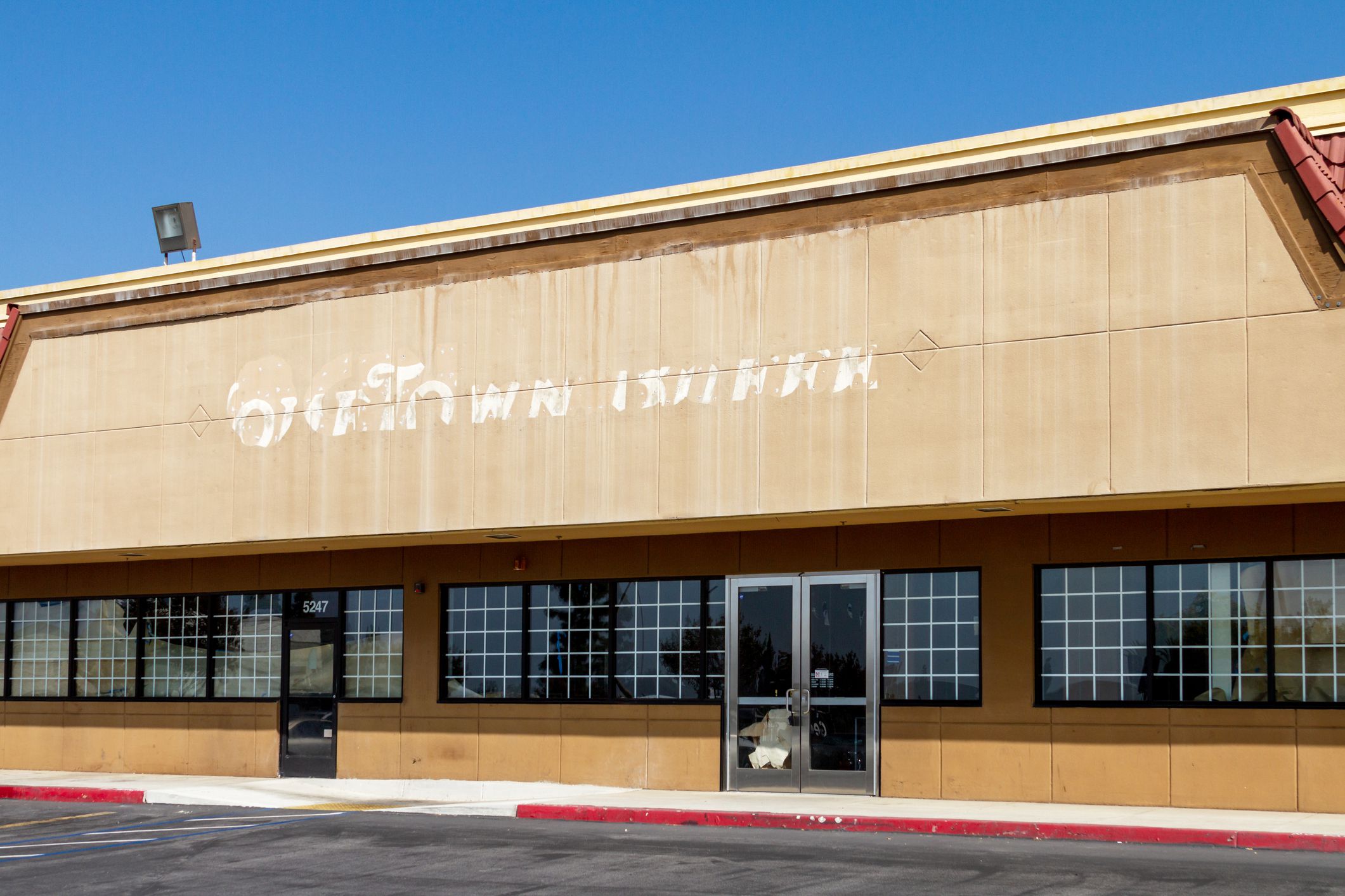 Front exterior of an abandoned building for the HomeTown Buffet restaurant, Montclair, California, previous sign faintly imprinted on it, empty parking spaces in the foreground and blue sky in the background