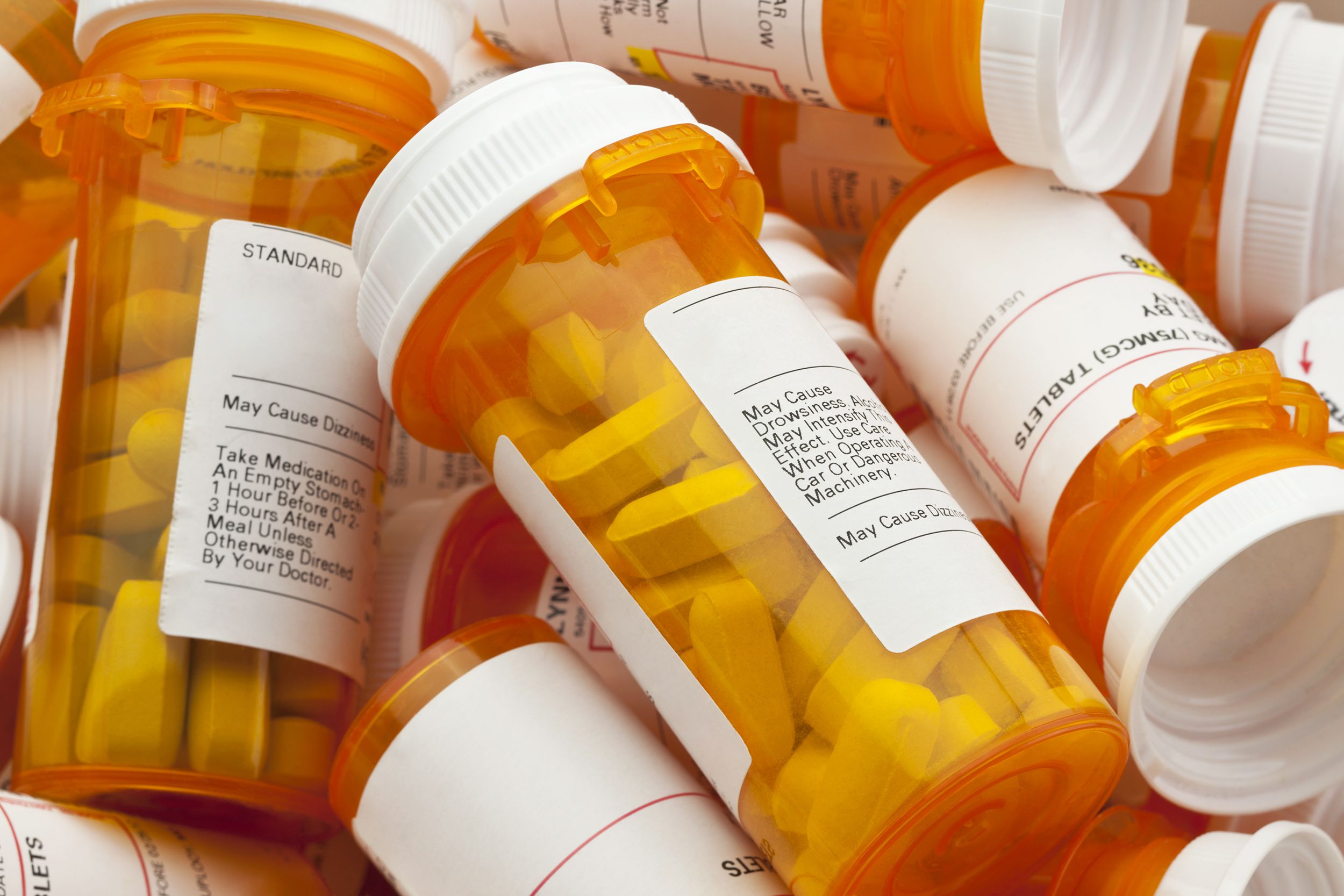 Closeup of a pile of prescription bottles of large pills, orange bottles with white caps and official prescription labels