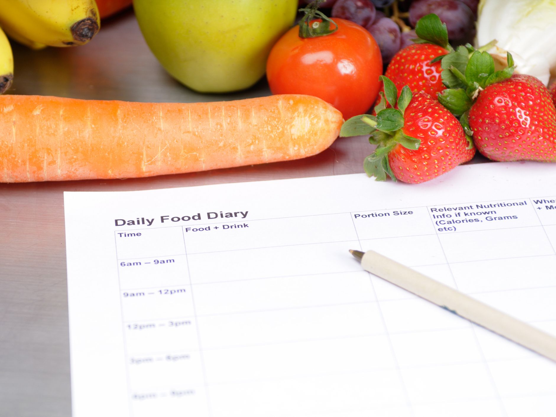 A food diary on a table surrounded by fruits and vegetables.