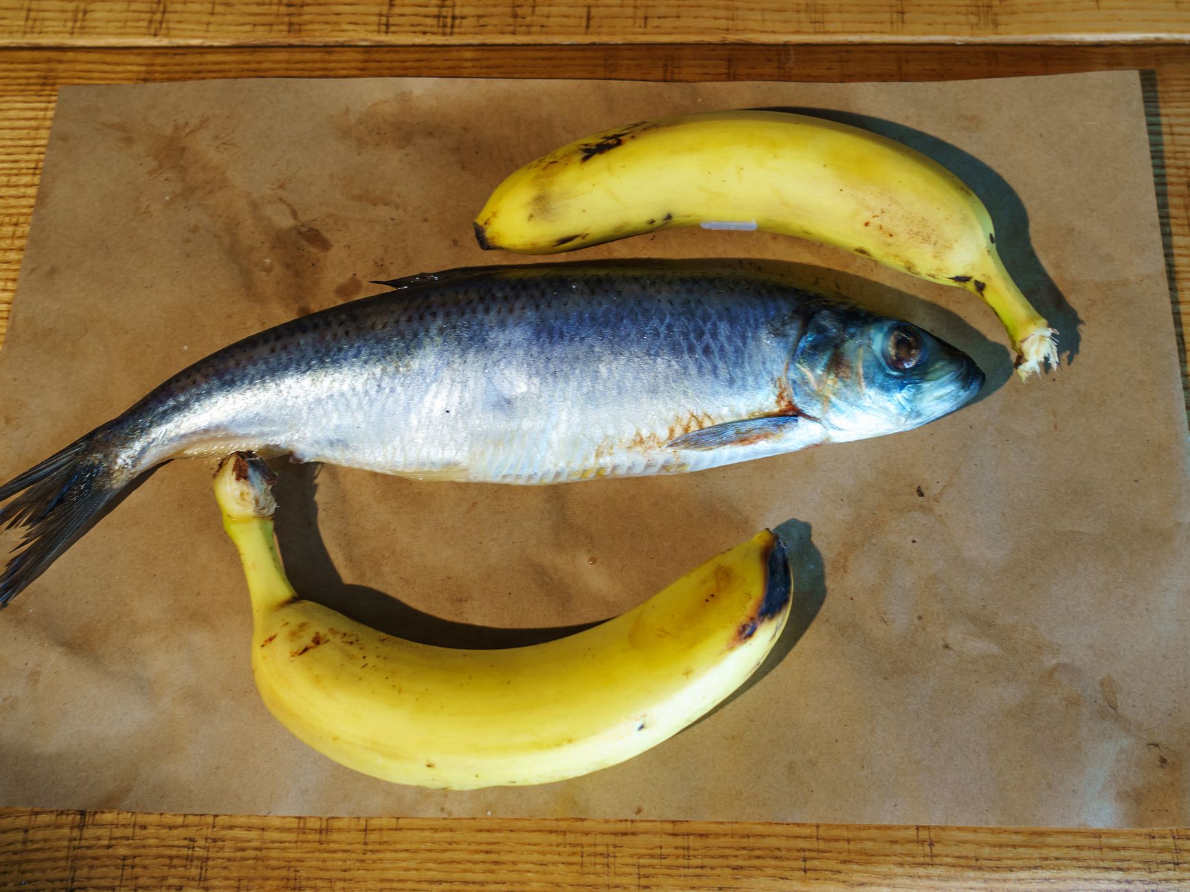 Close-up delicious salted herring and two yellow bananas on the old wooden background. Rustic style.