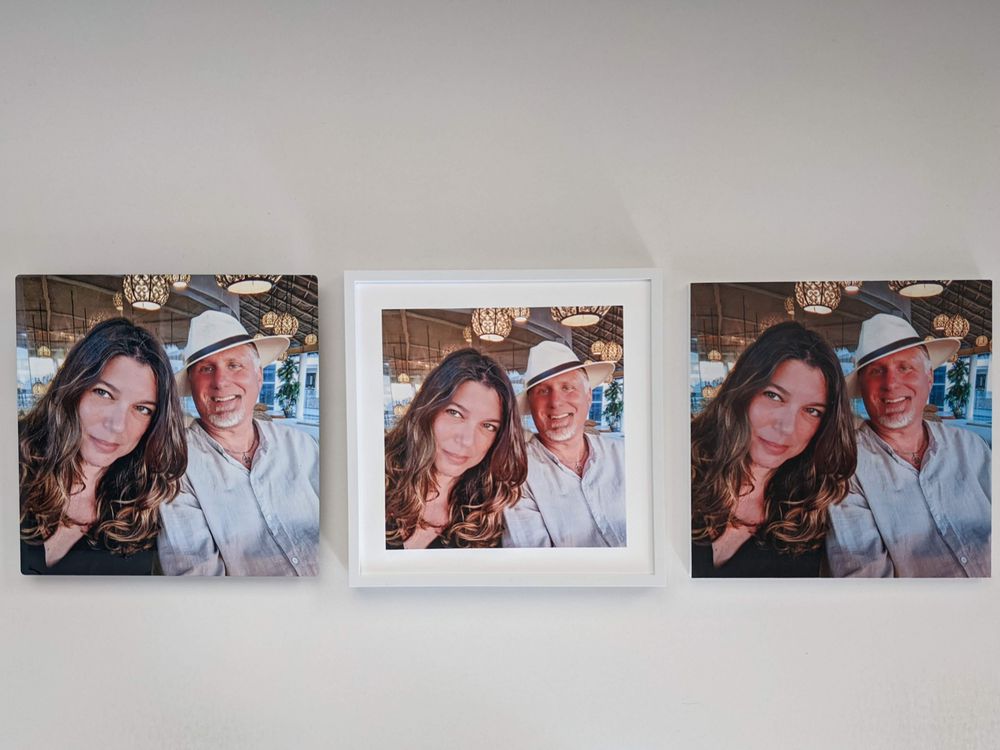 Three framed photos hang on a white wall, each showing the same image of a woman with long brown hair and a man in a white hat and shirt sitting together and smiling at the camera.