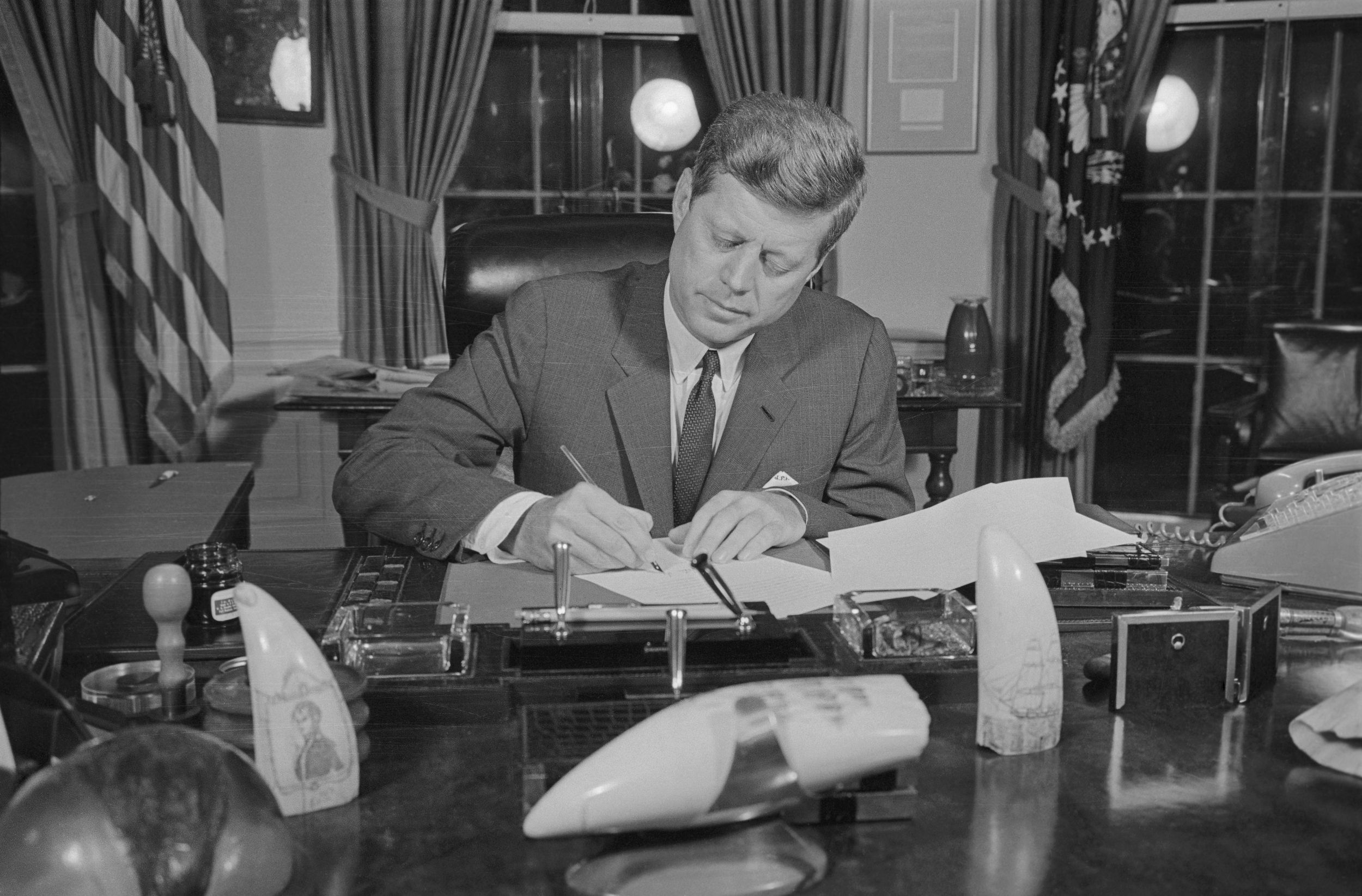 President John F. Kennedy signing blockade order at his desk in the Oval Office, the White House, 1962, black and white image