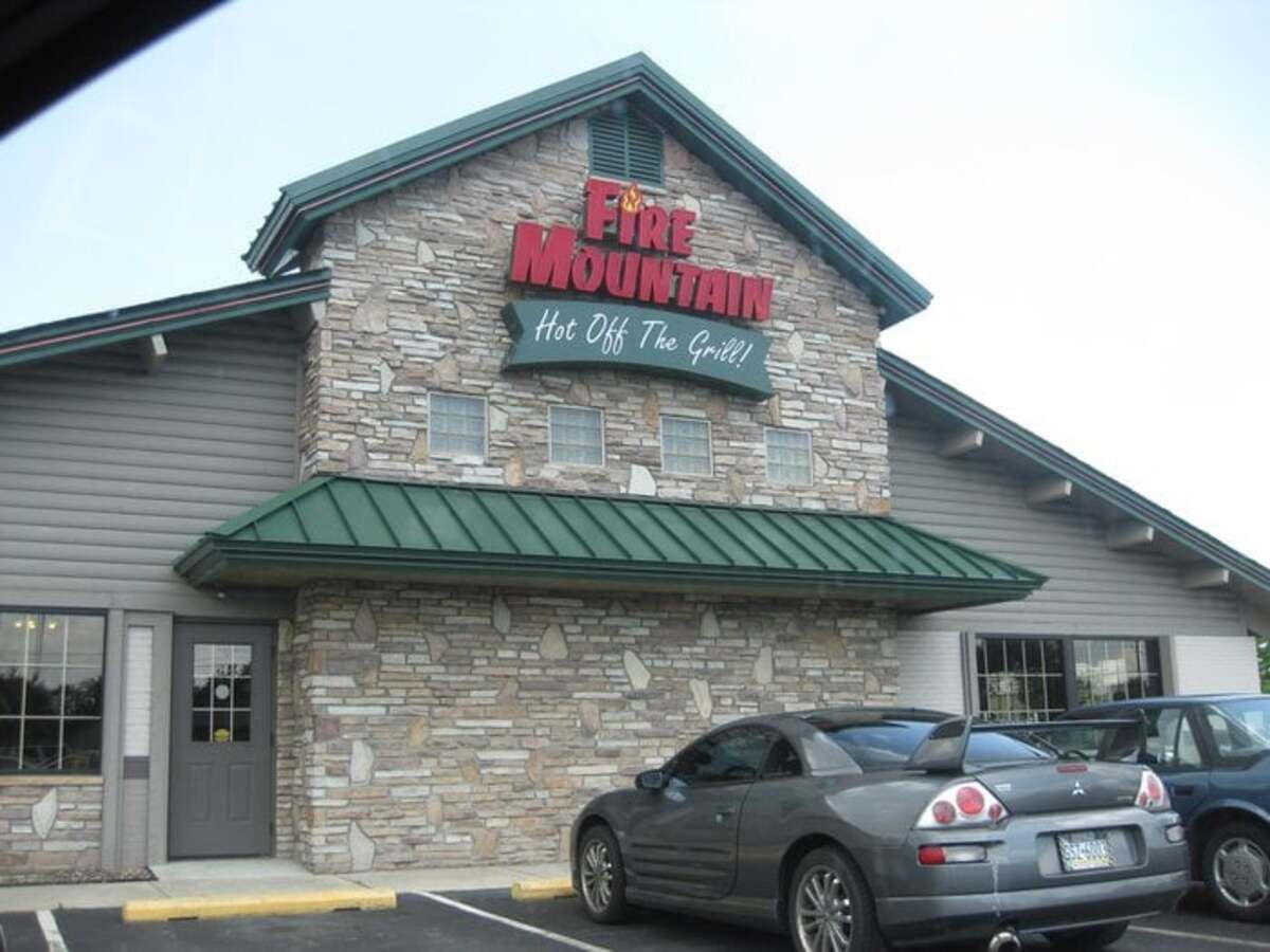 Side exterior of Fire Mountain, Mechanicsburg, Pennsylvania, parking spaces in the foreground with two cars parked on the middle and right, a light blue sky in the background