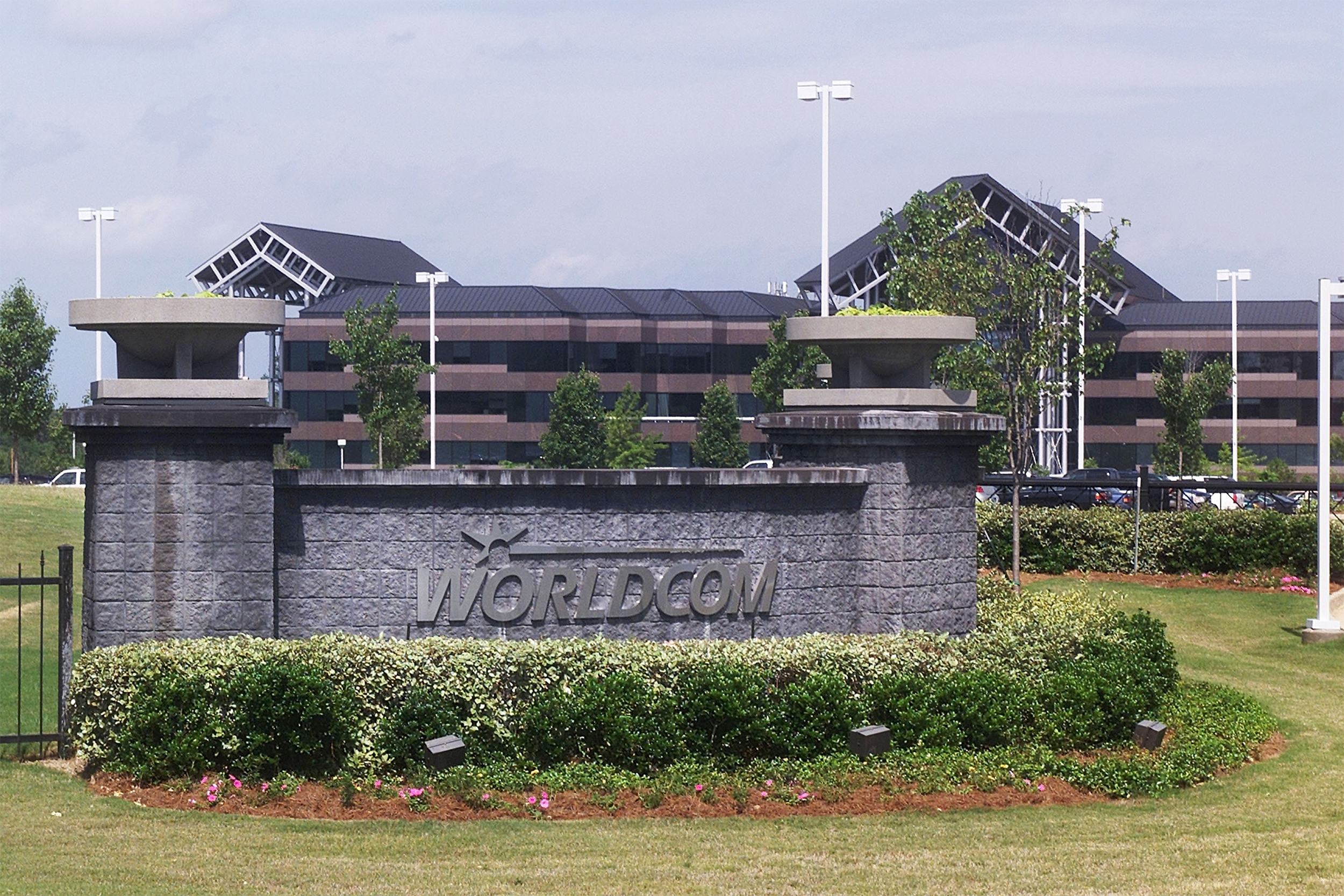 Sign of WorldCom Inc. In front of exterior of building, Clinton, Mississippi, sign is surrounded by bushes, cars are parked in the parking lot in front of the building, on a sunny day, a blue sky with clouds in the background