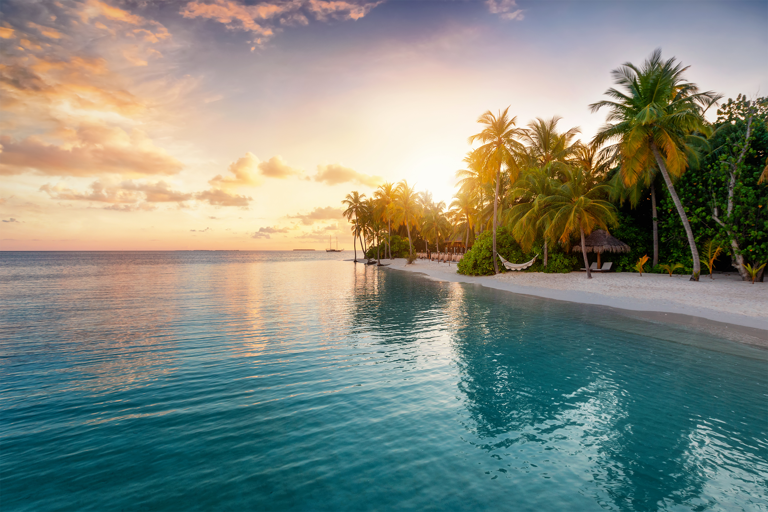 Sunrise behind palm trees on a tropical island in the Maldives, sandy beach and clear ocean, a boat on the horizon