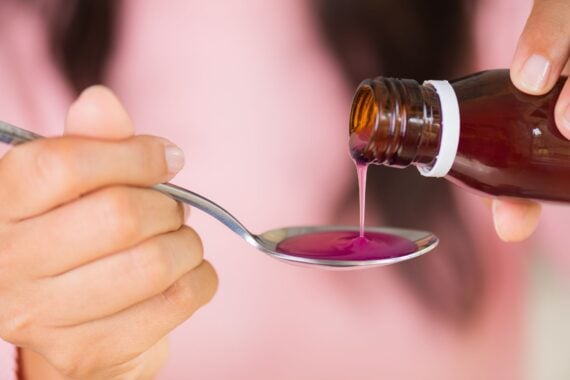 Woman hand pouring medication or antipyretic syrup from bottle to spoon. health care, people and medicine concept.
