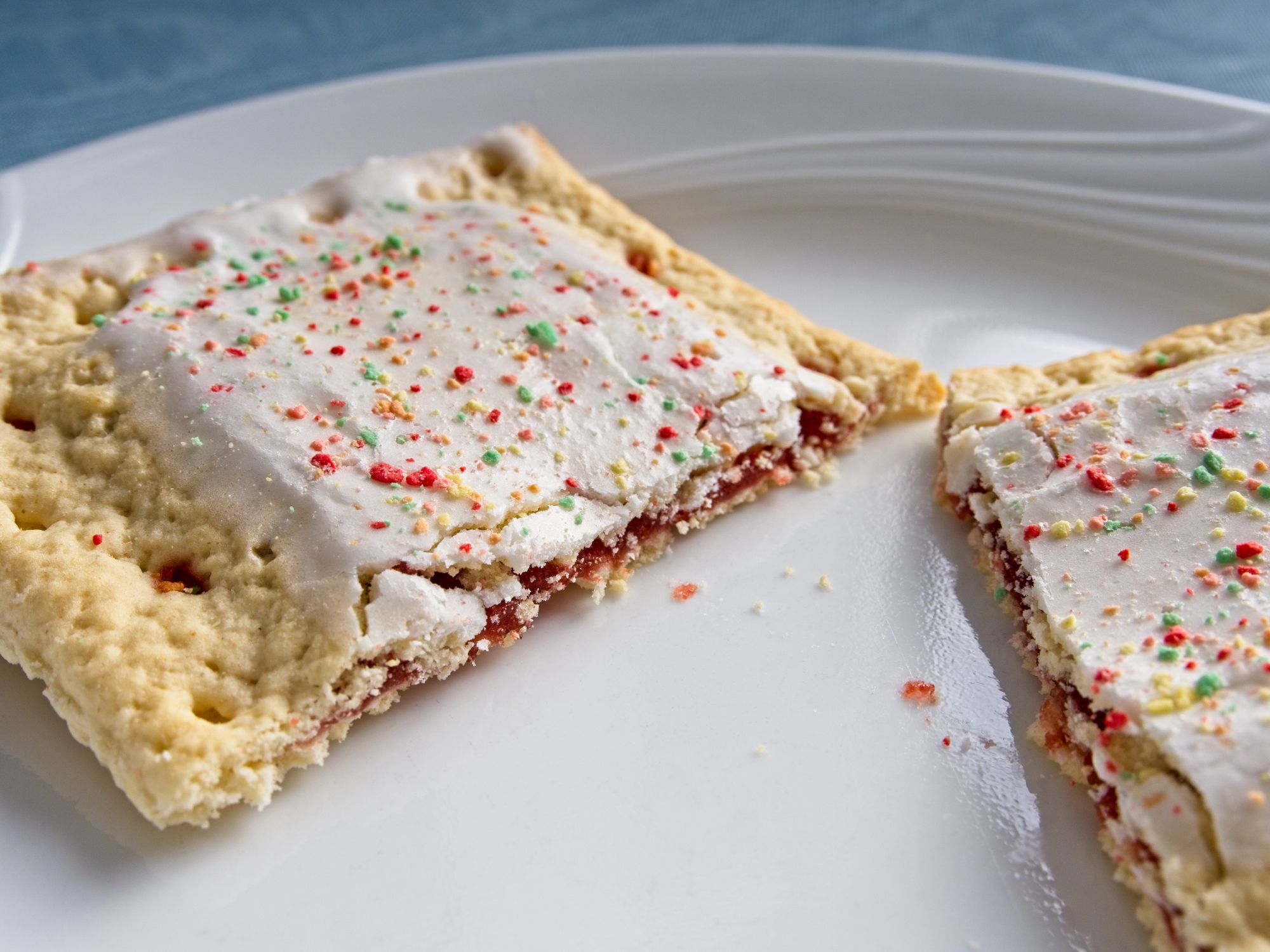 Sweet toaster pastry on white plate and blue tablecloth background. A common quick breakfast item that is tasty, filling with plenty of calories, but with less than ideal nutritional value.
