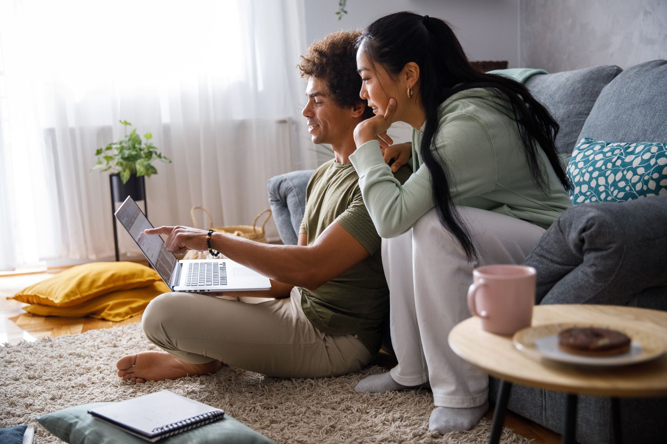 Wide shot of millennial couple lounging in their living room, planning out their finances and looking at their account via online banking.