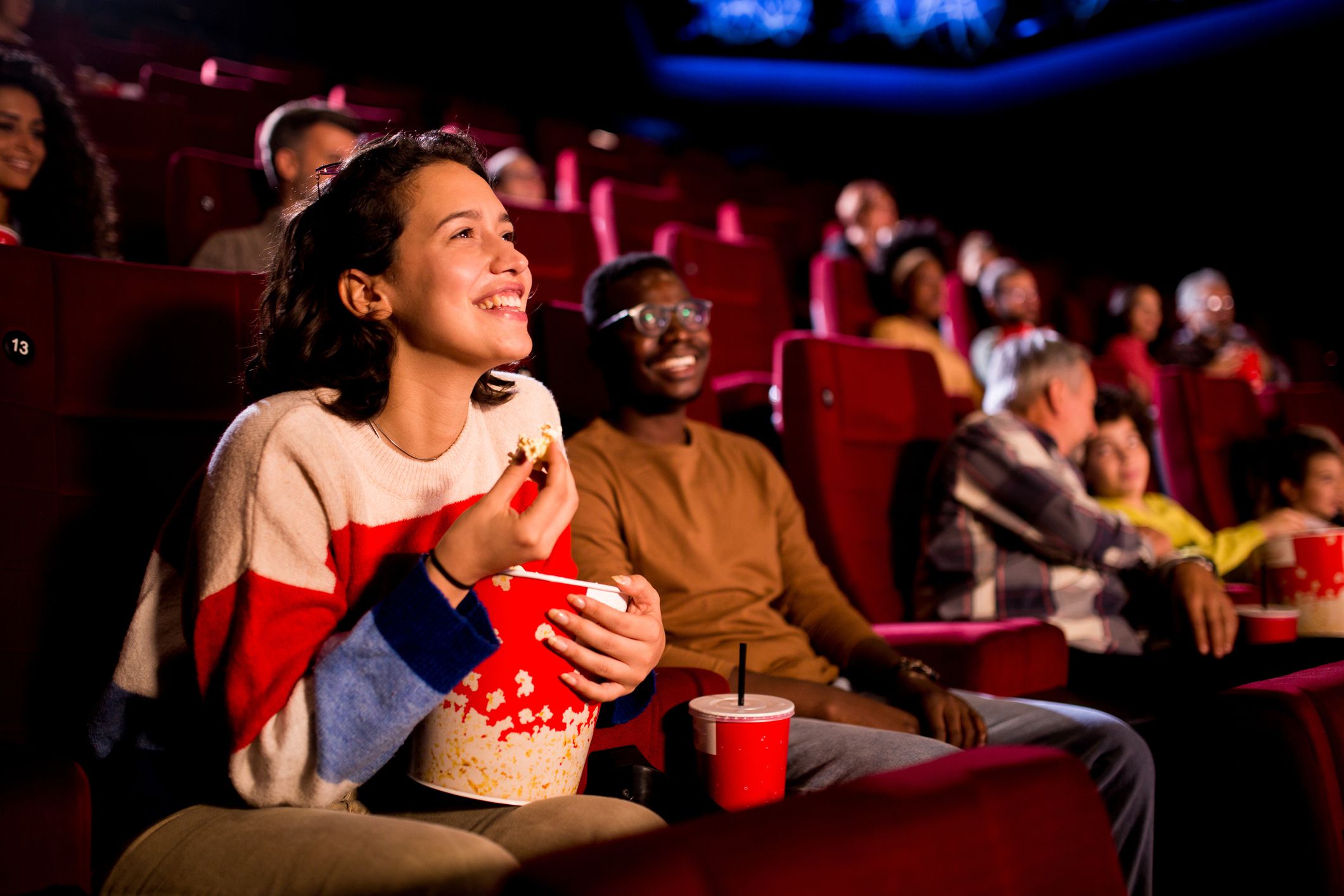 Girl watching a comedy movie at the cinema with her African American friend.