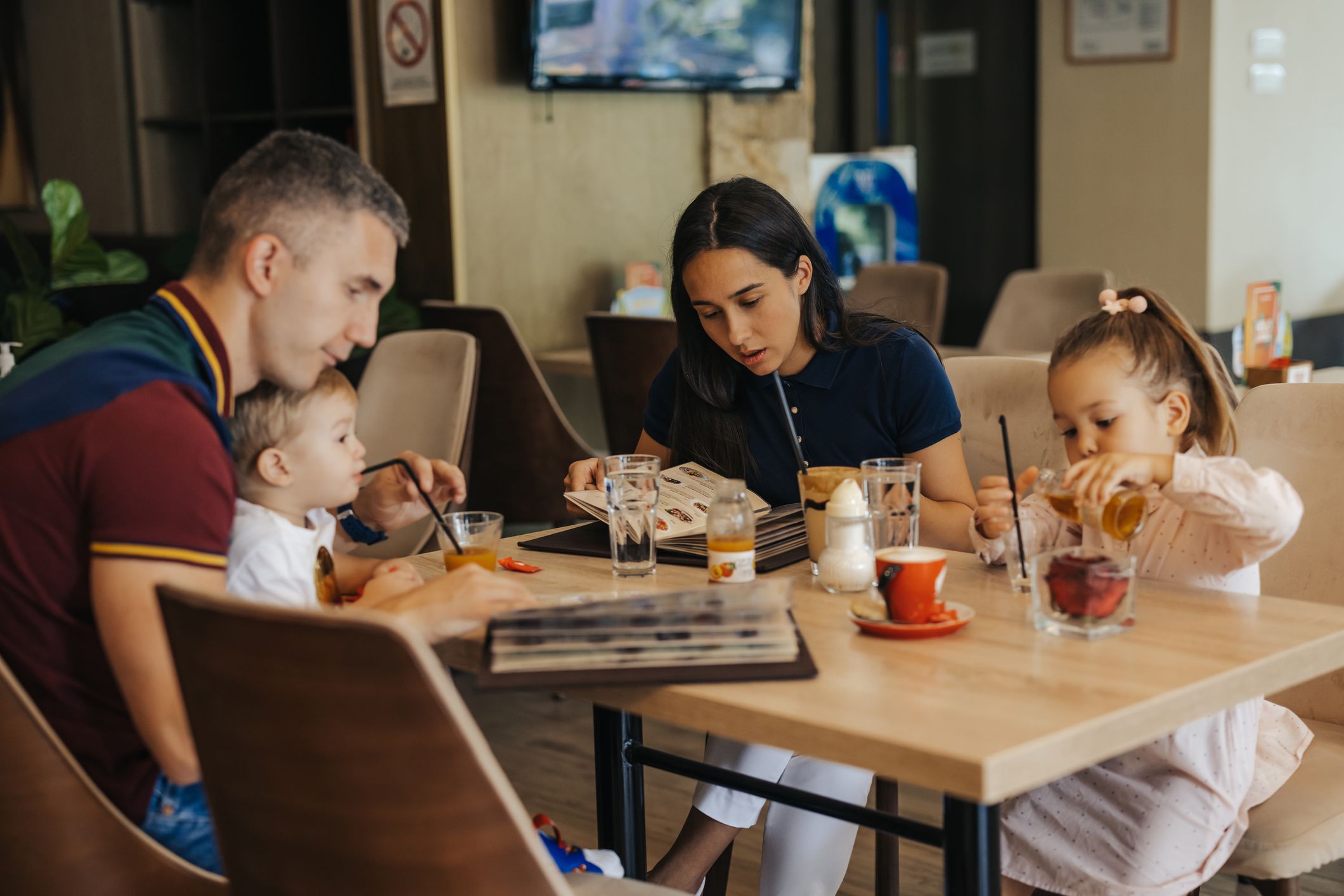 Young family, husband, wife and two kids, son and daughter enjoying drink and time together at restaurant, looking at menu and preparing to order the food