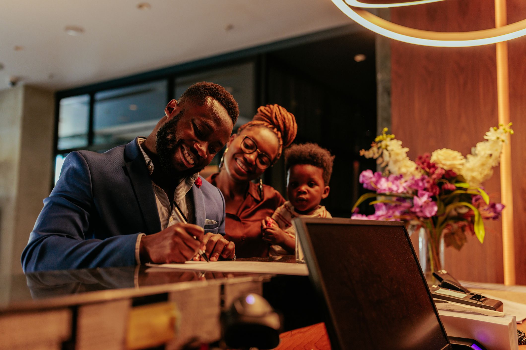 A happy African American family is at the front desk in the hotel. They are signing into the hotel guest book happy with they stay at this luxurious establishment.