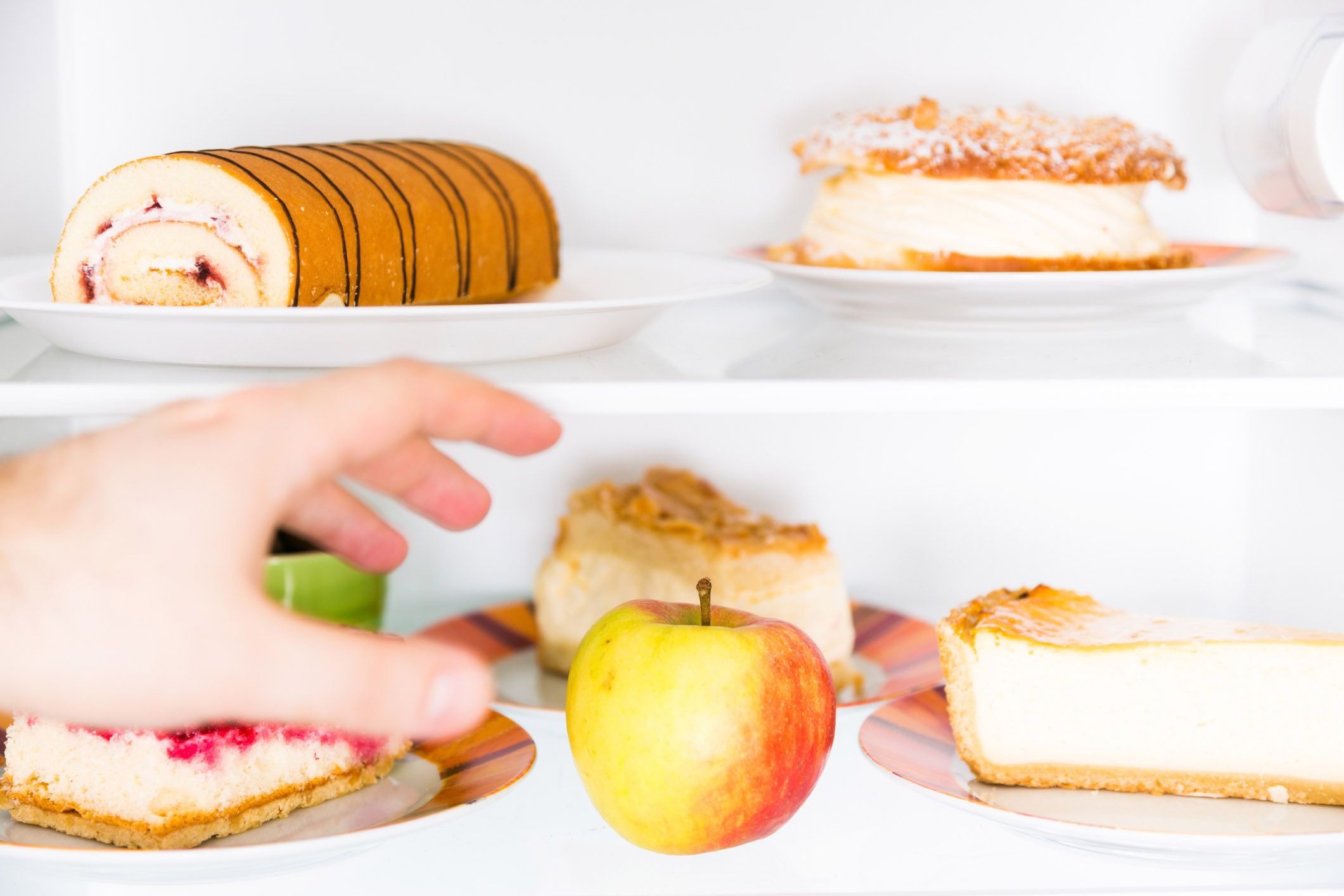 hand reaching for cakes in fridge