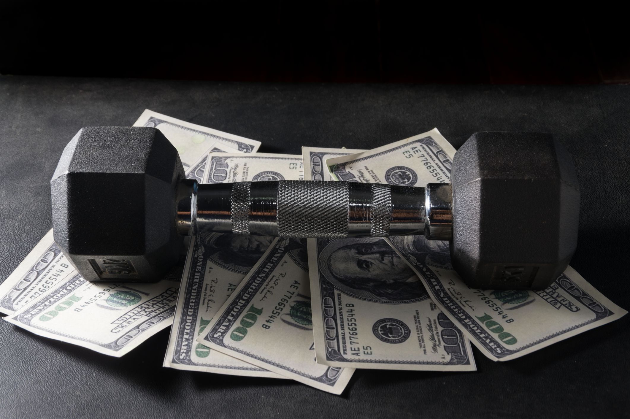 Metal dumbbell on dollar bill.