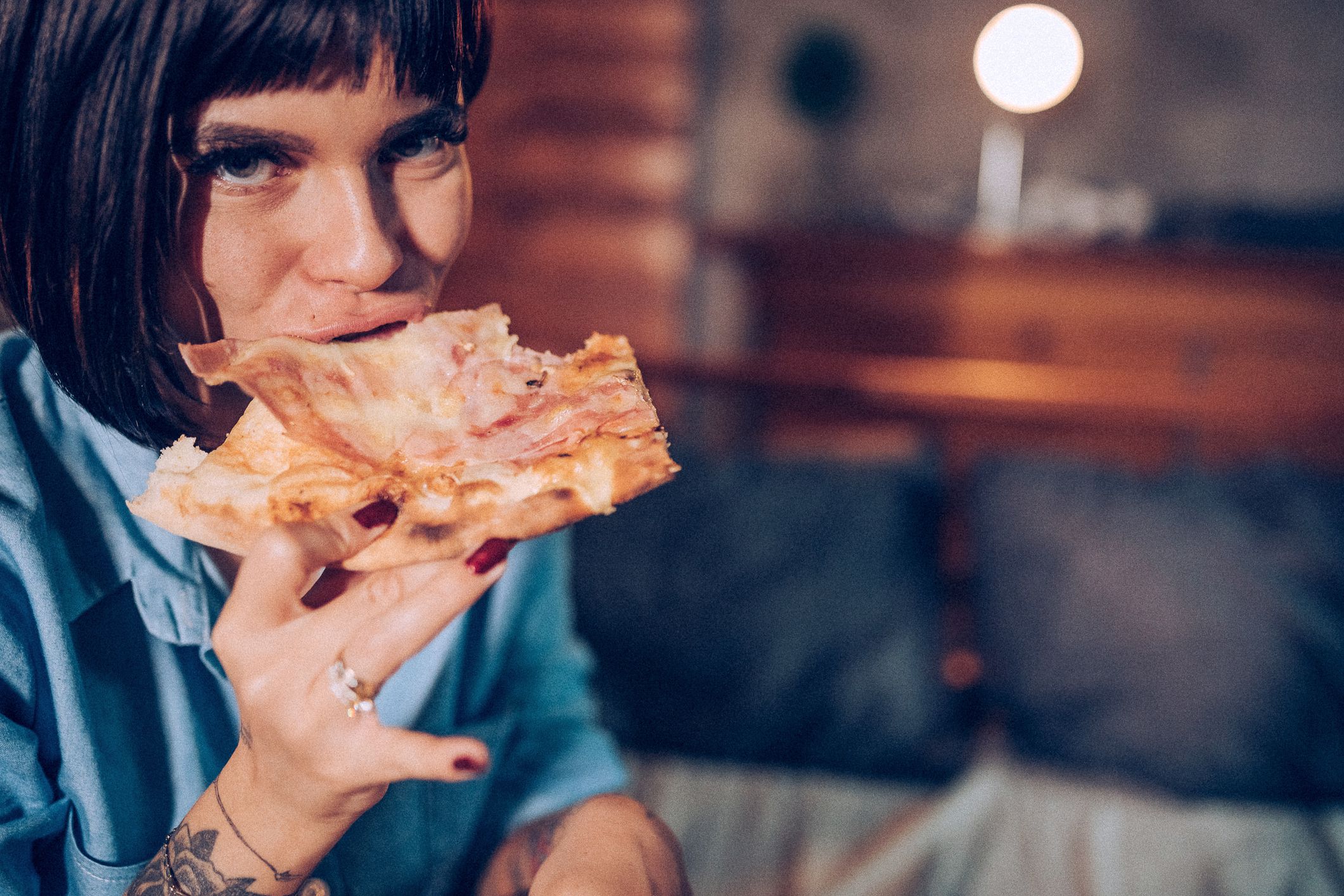Lonely tattooed woman eating pizza in bed