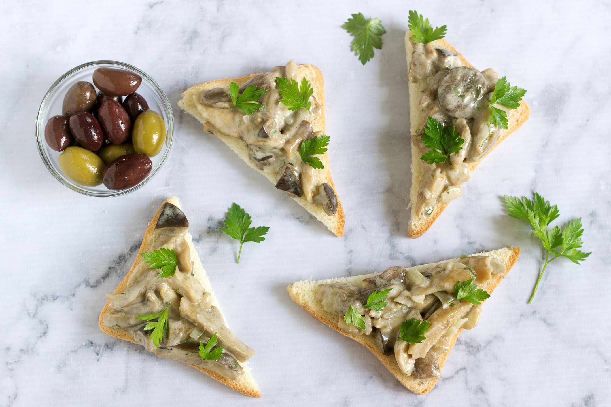 Triangular sandwiches with summer mushrooms cooked with cream and herbs served with olives. Selective focus.