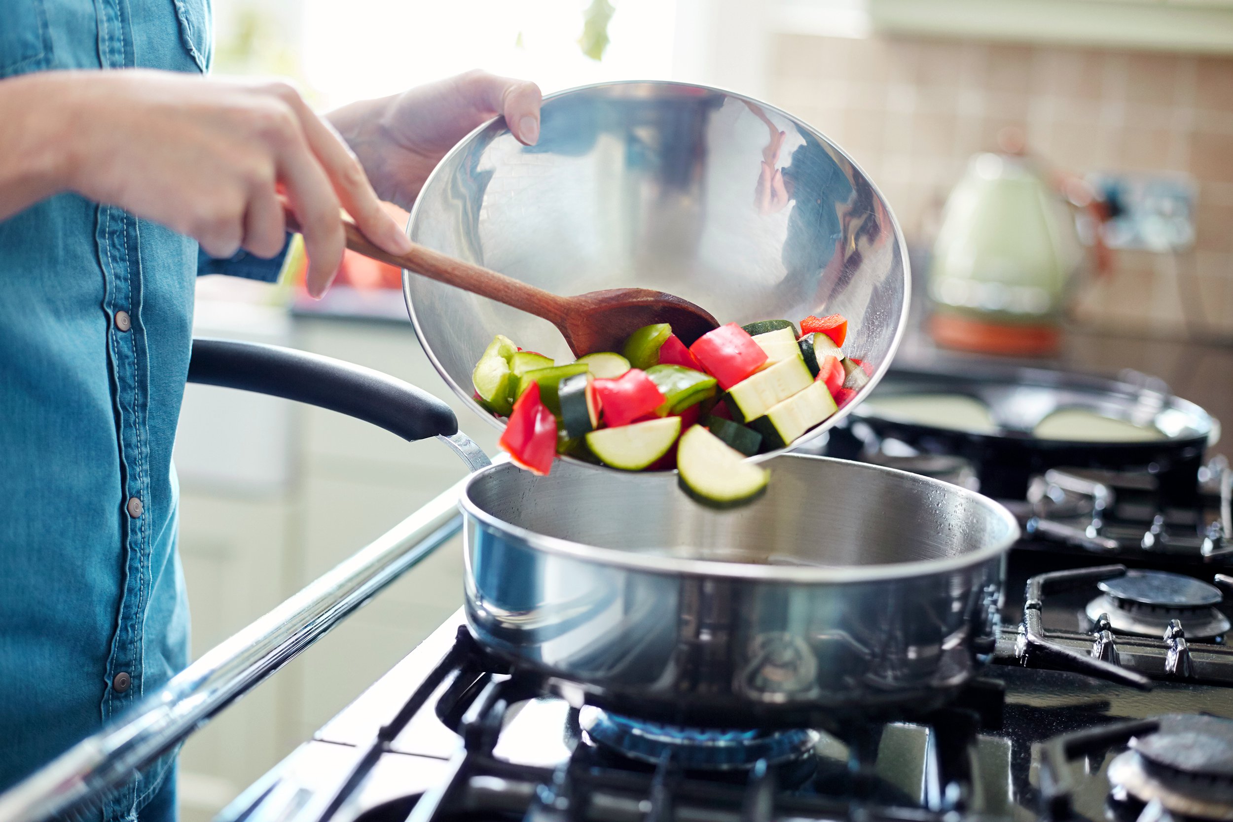 Woman pouring fresh vegetables into a frying pan