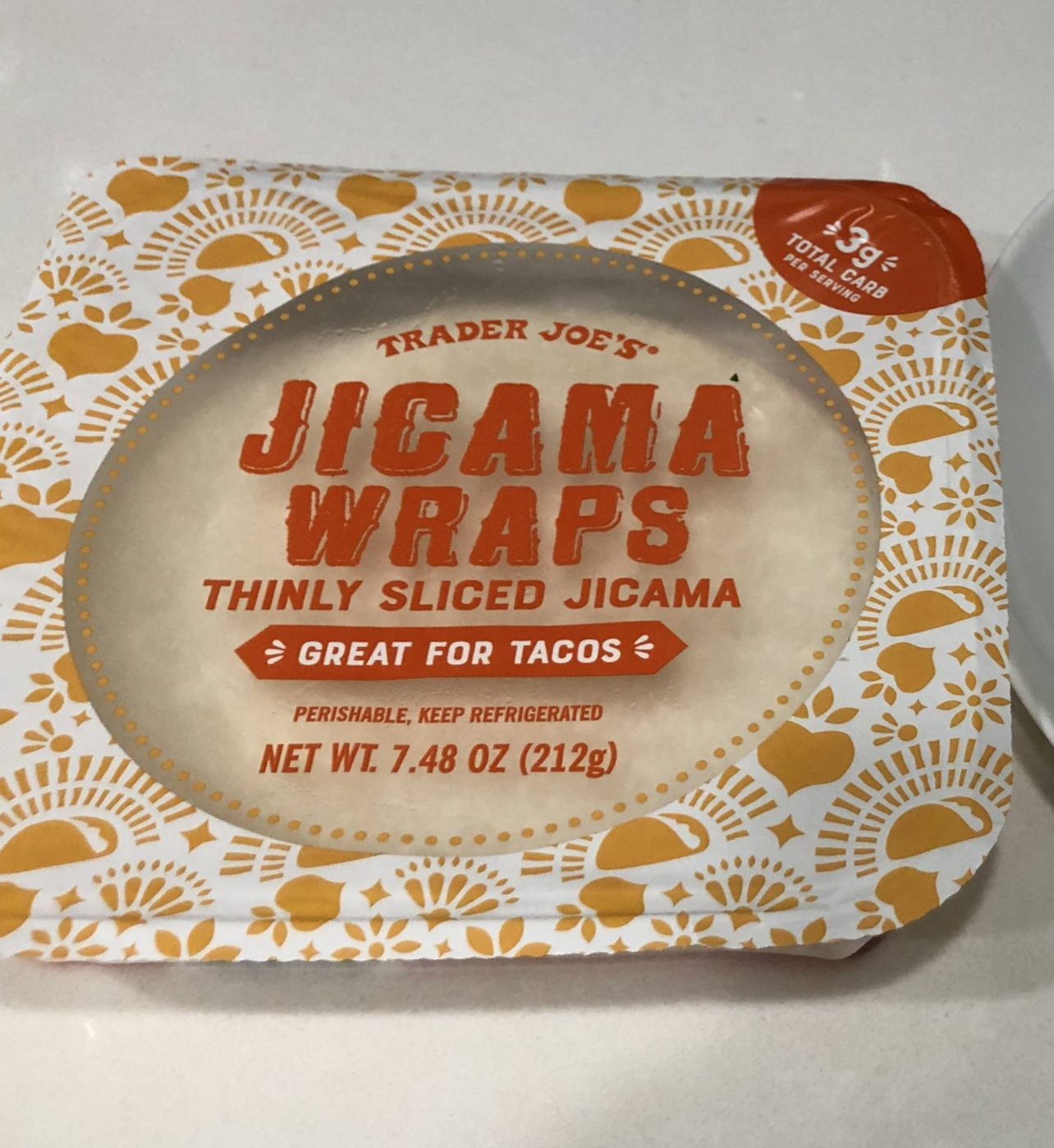 Trader Joe’s Jicama Wraps package, labeled “Thinly Sliced Jicama - Great for Tacos,” with an orange and yellow decorative border. The net weight is 7.48 oz (212g), and it shows 1.9g total carbs per serving.