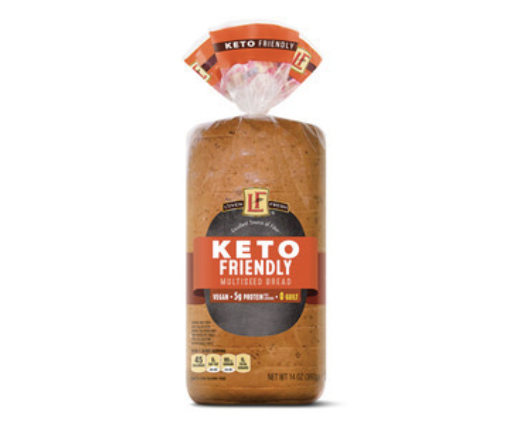 A loaf of keto-friendly multiseed bread in clear packaging with a black and red label, showing nutrition highlights and branding. The bread is upright on a white background.