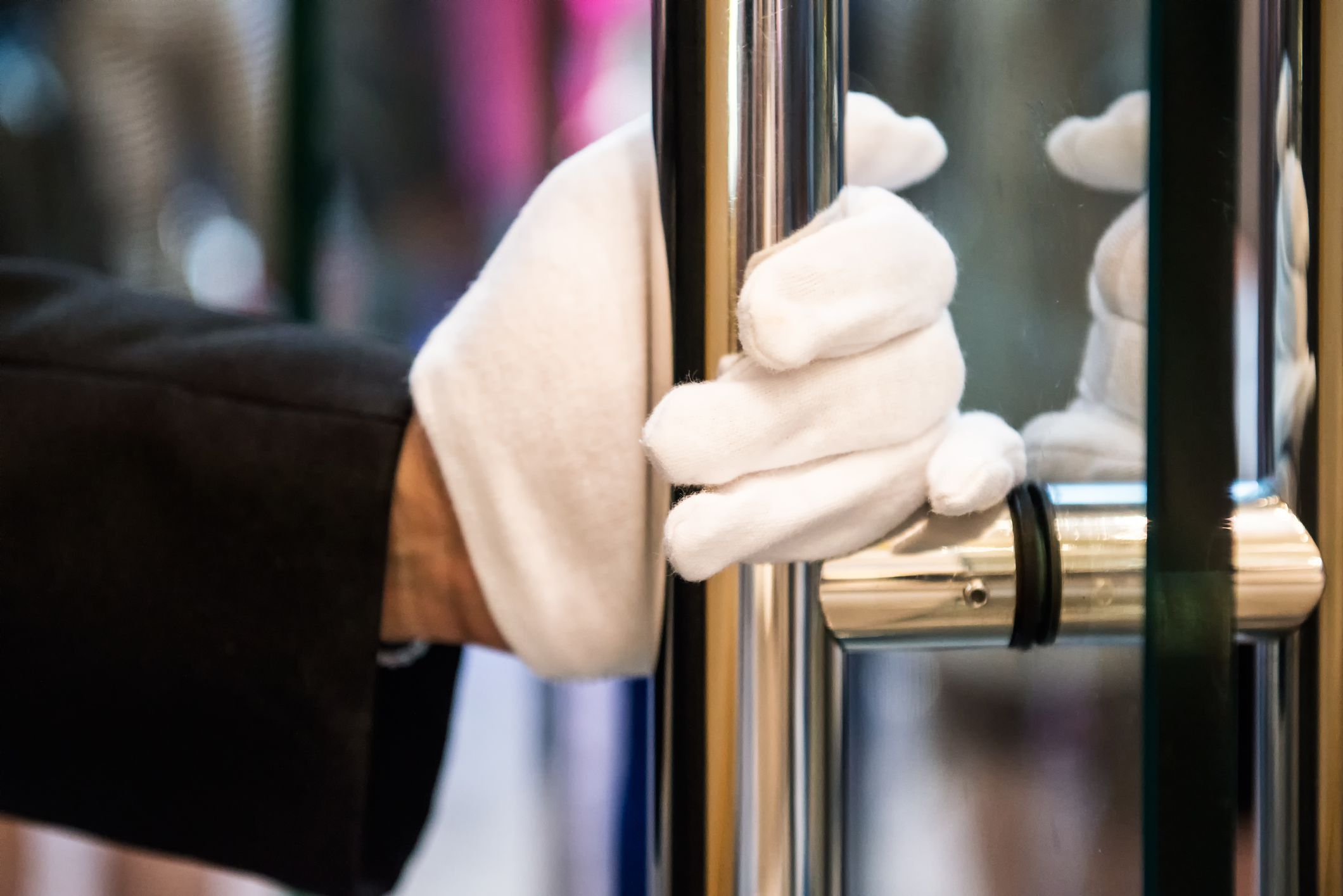 Closeup doorman with white gloves holds a brass handle to a glass door at an expensive hotel in Hong Kong