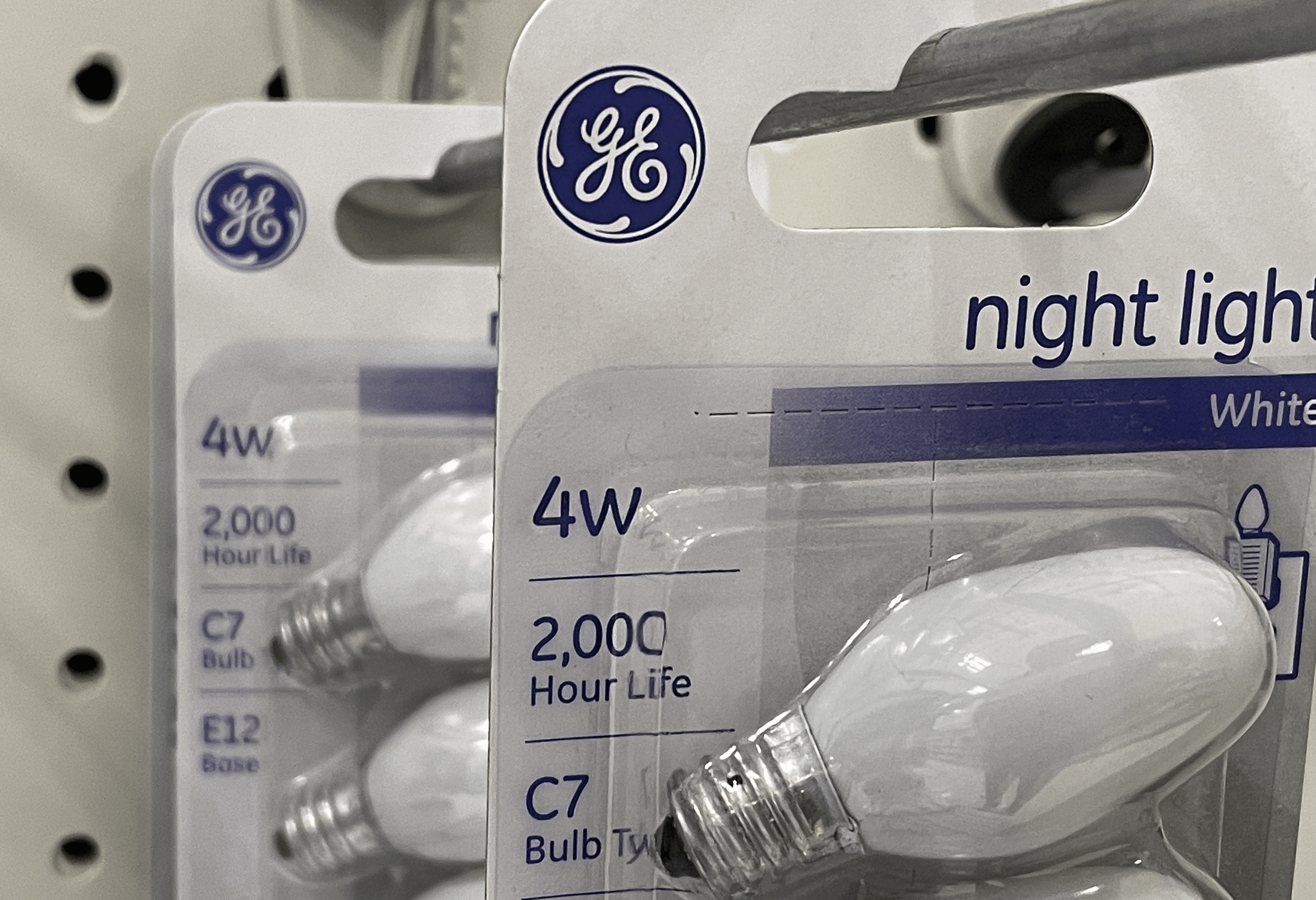 Closeup of three packages of General Electric light bulbs are displayed on a shelf at a Target store, San Rafael, California, hanging on a metal, white metal background