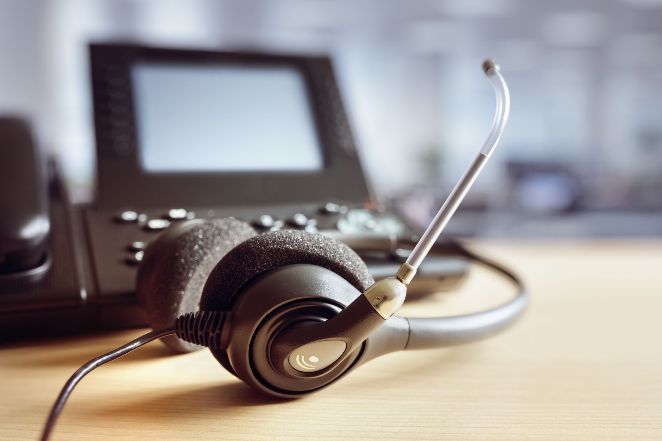 Closeup of headset and telephone for telephone operator on desk, blurred background
