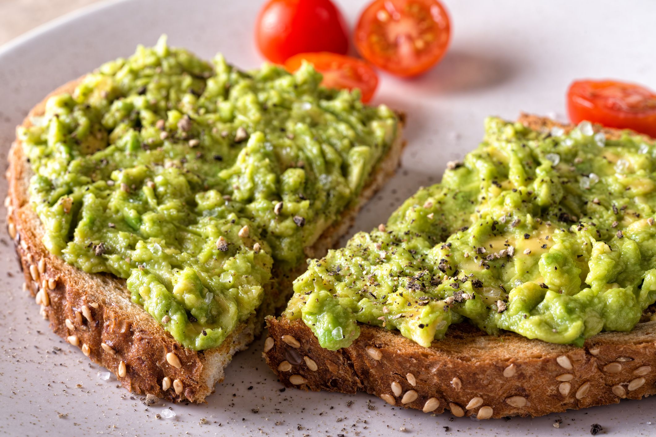 Closeup of two slices of avocado toast on a white plastic plate with cherry tomatoes