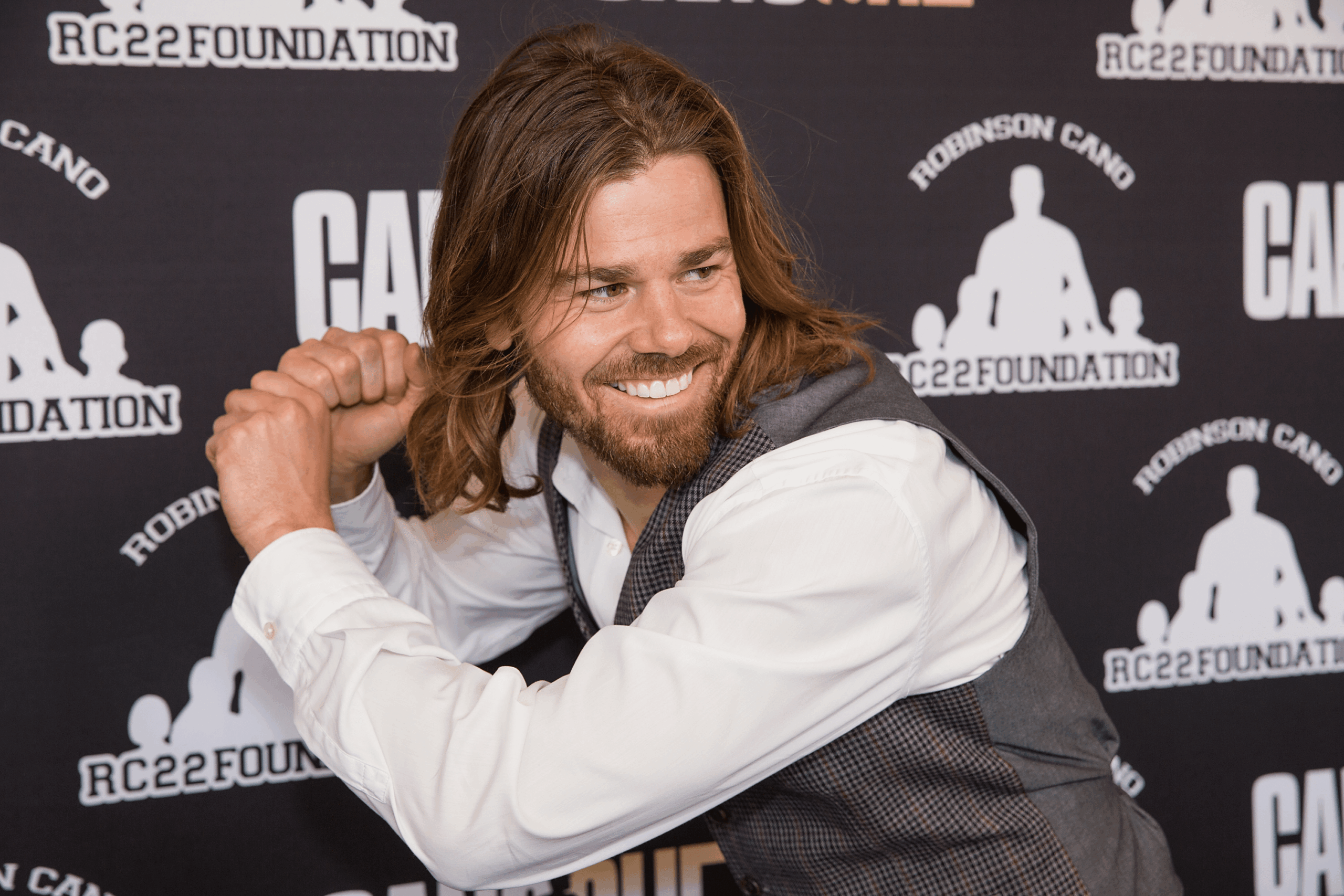 Dan Price smiling and making a baseball batter gesture, attends the Canoche Benefit for the RC22 Foundation At the Paramount Theatre, Seattle, 2015, dark purple background with RC22 Foundation logo