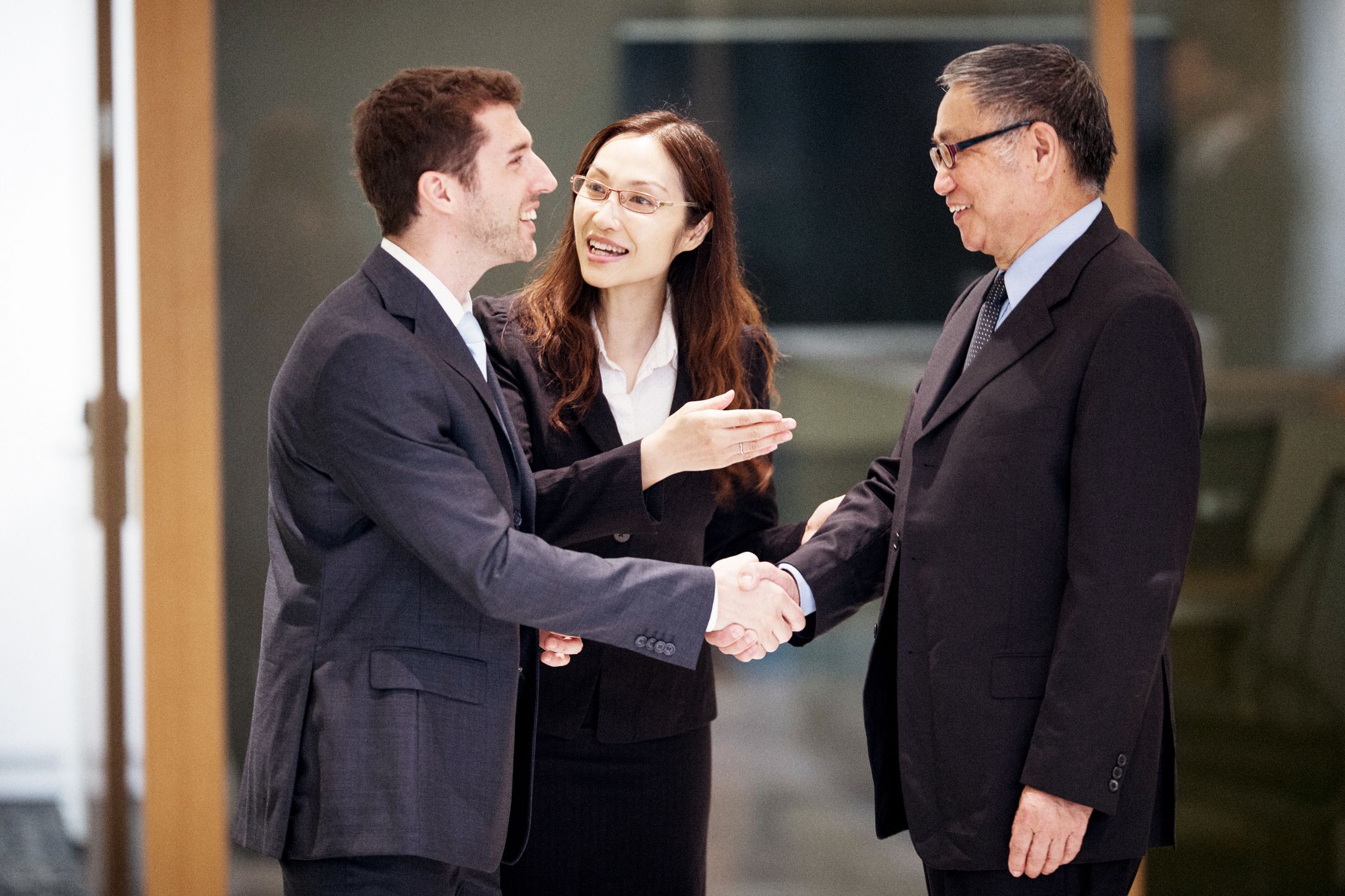 Businessman speaking English closing a deal in Hong Kong with his male colleague speaking chinese, female translator standing between them facilitating conversation, blurred background