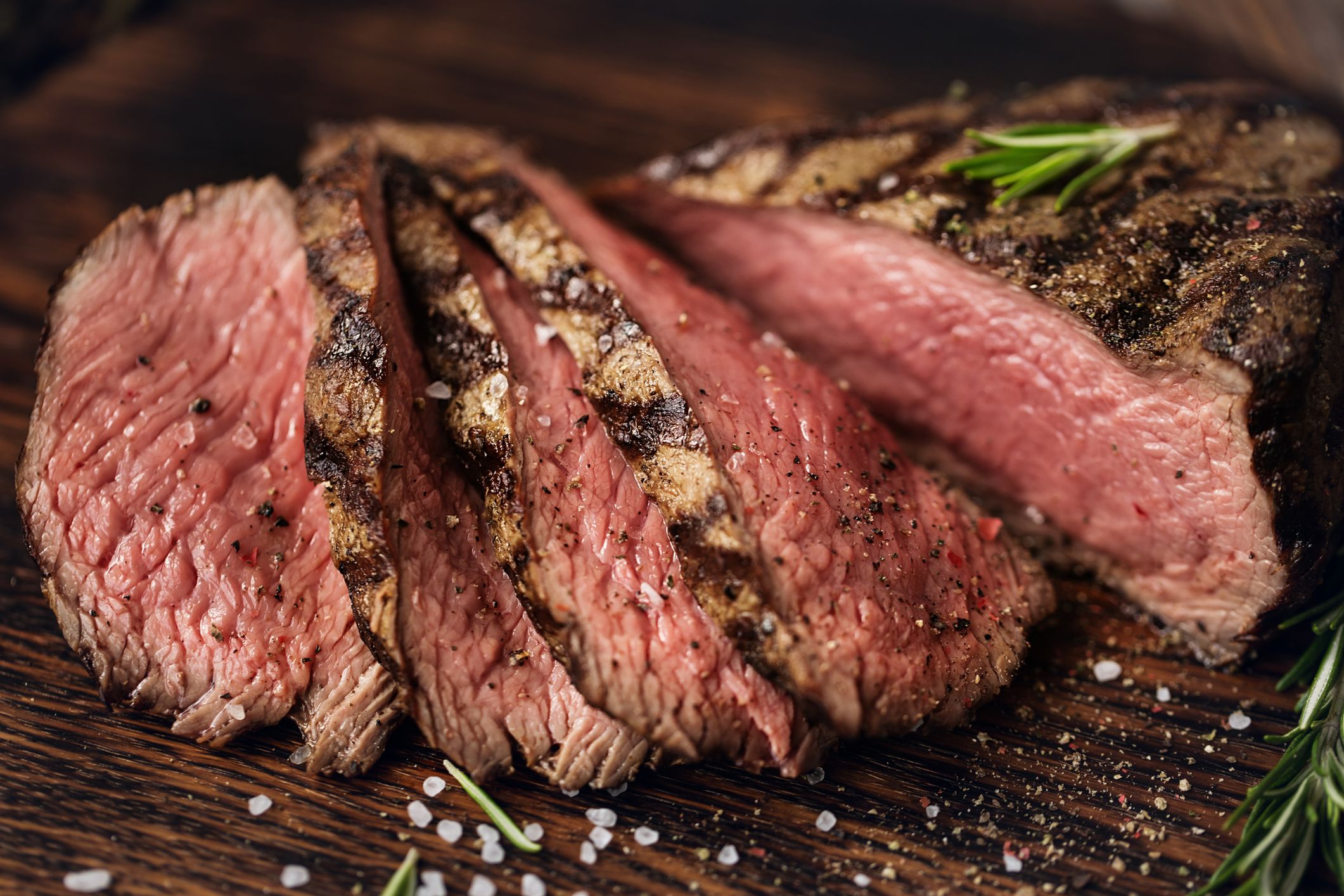 Focus on slices of a juicy medium beef rib eye steak with salt and herbs on an artisanal cutting board