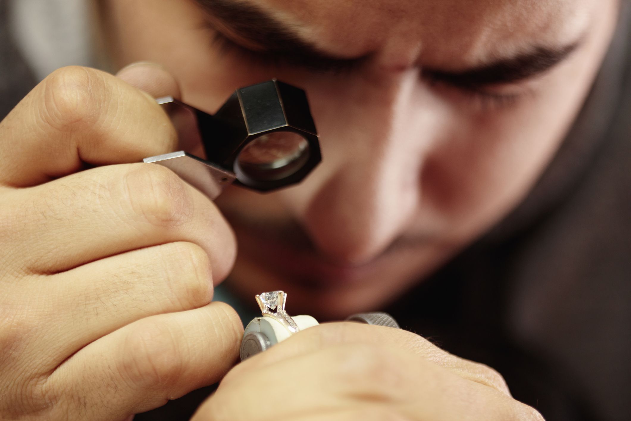 Male jeweler inspecting diamond ring with magnifying glass closeup