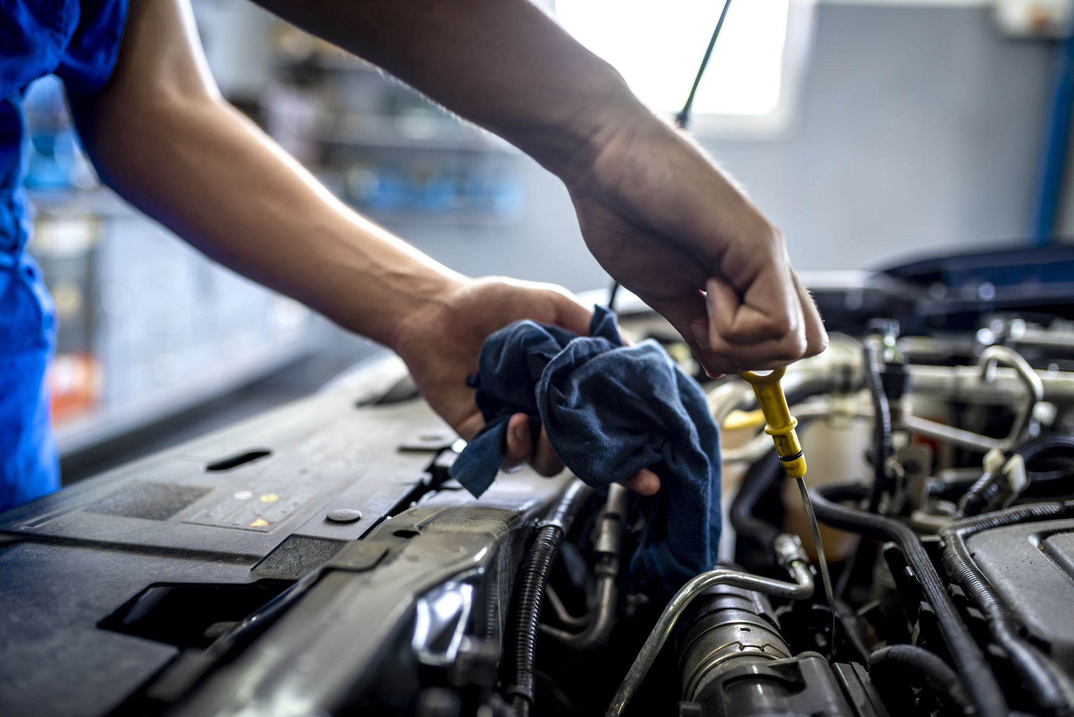 Male mechanic measuring the oil level of an engine at an auto shop, closeup of mechanic pulling out oil dipstick, blurred background