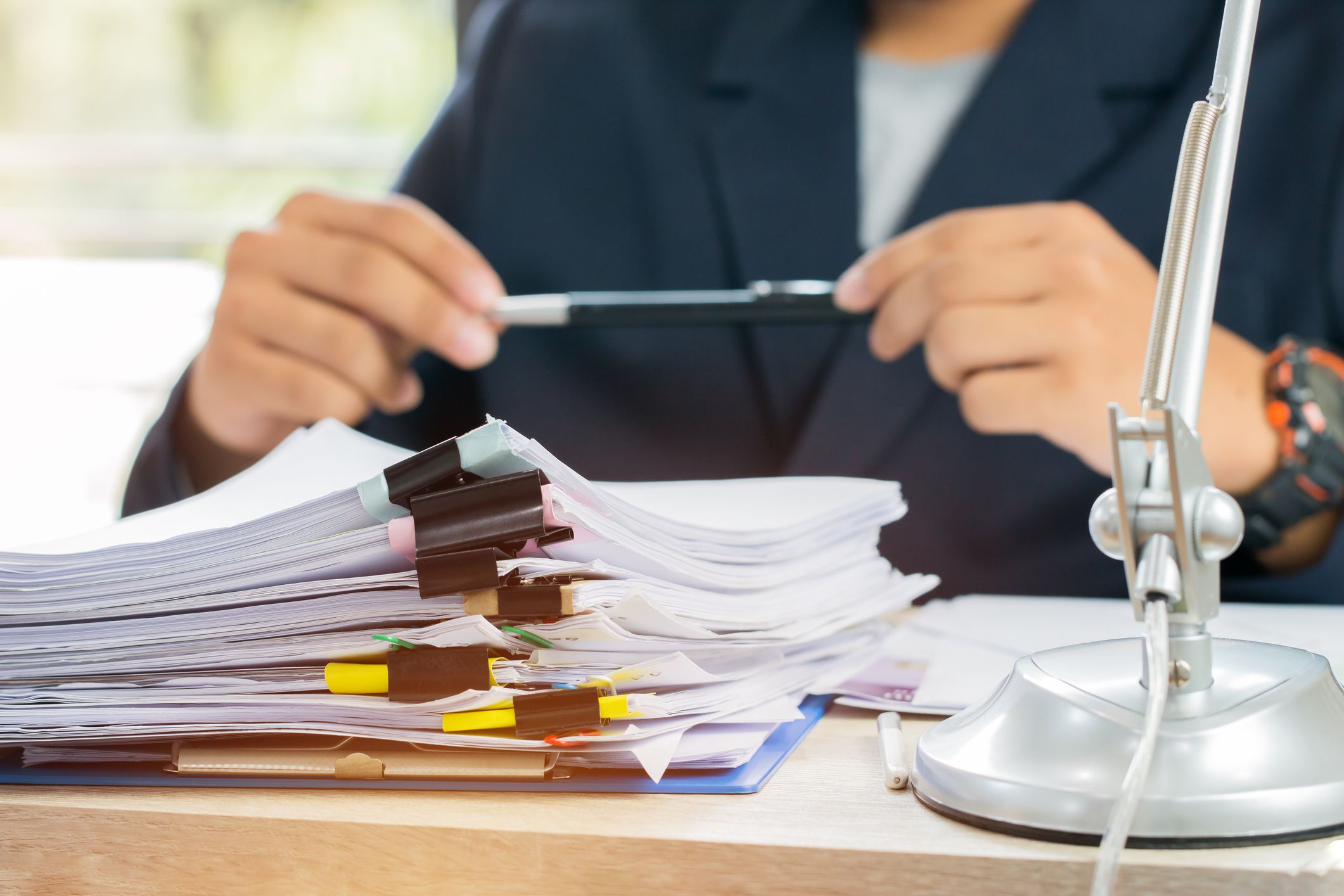 Male paralegal with a stack of legal documents on desk, holding pen with both hands