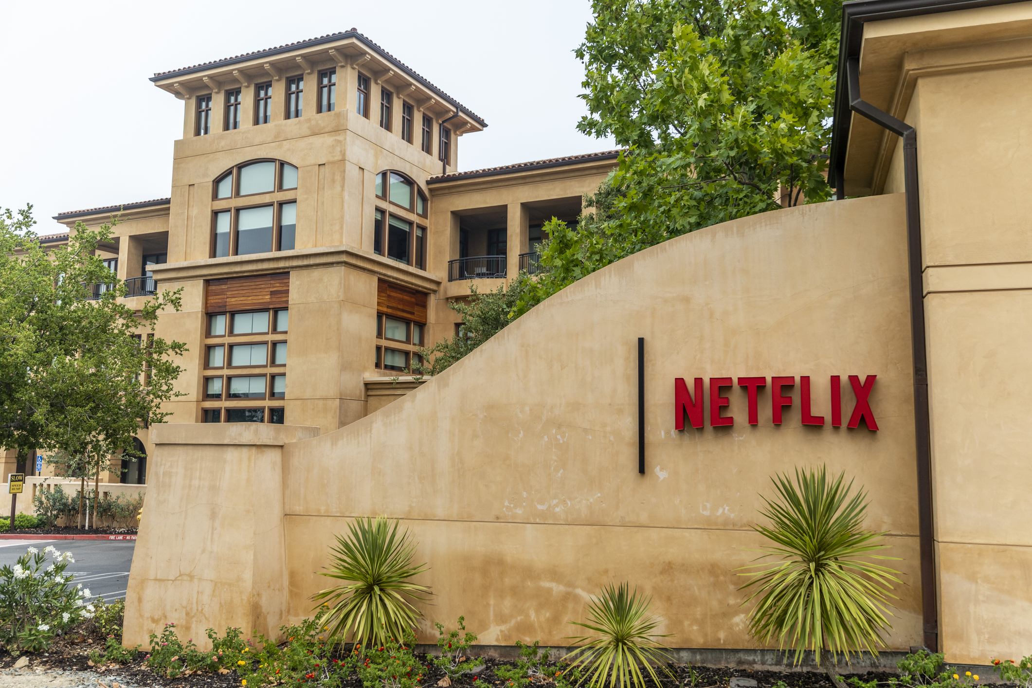 Stone front gate in the foreground with tropical plants, Netflix Headquarters, Los Gatos, California, building in the background against a light blue sky