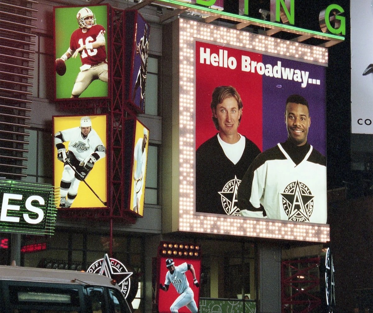 A large billboard in Times Square shows two men in black-and-white hockey jerseys with the text "Hello Broadway..." Next to it are images of an American football player, a hockey player, and classic ads from old restaurant chains.