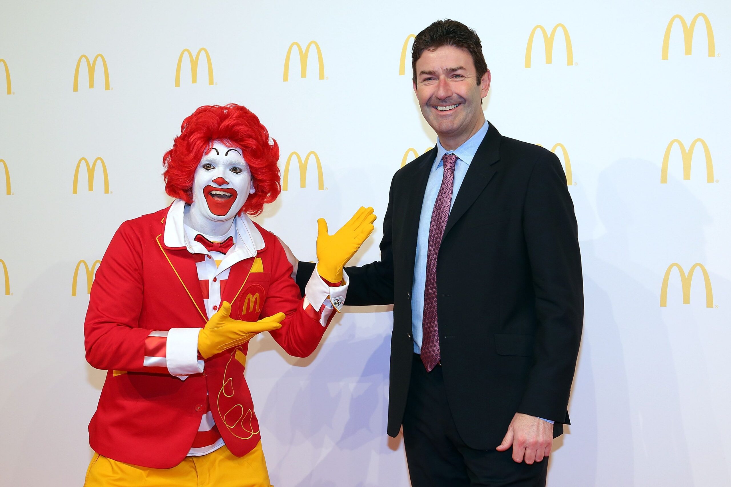 Steve Easterbrook poses with Ronald McDonald during the new McDonald's flagship restaurant re-opening at Frankfurt International Airport, Germany, yellow McDonald’s logo on a white background