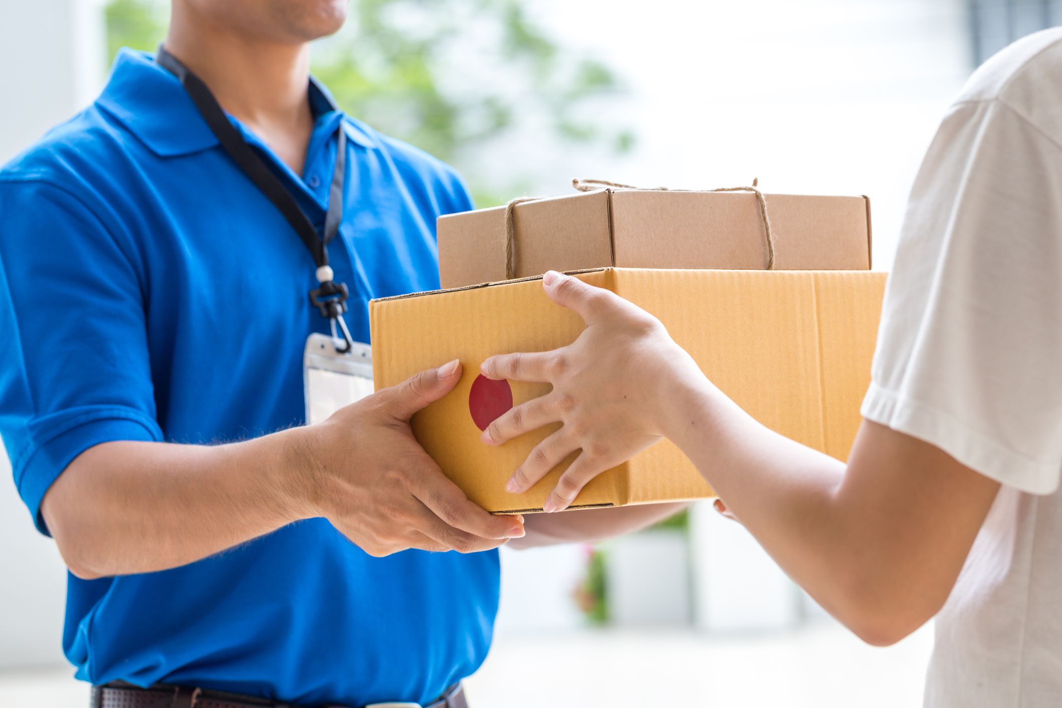 Woman's hands accepting a delivery of boxes from a delivery man who is wearing a blue shirt, woman is showing backside, blurred background