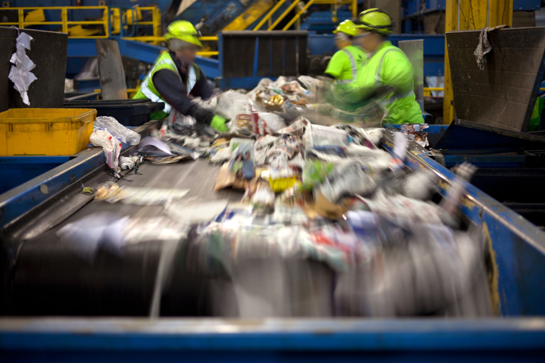 Workers separating paper and plastic on a conveyor belt in a recycling facility, closeup of items being sorting in motion