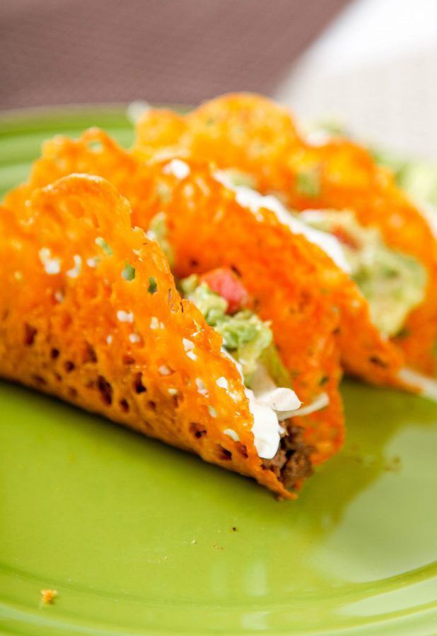 Two tacos with crispy, orange cheese shells filled with lettuce, guacamole, and other fresh toppings, served on a bright green plate.