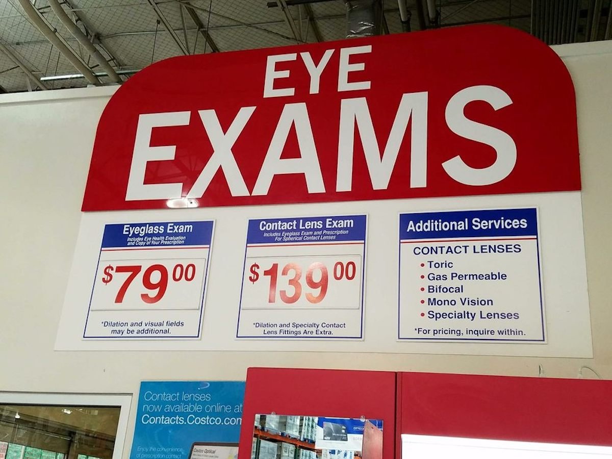 Large red and white sign reads “EYE EXAMS.” Below are prices: Eyeglass Exam $79, Contact Lens Exam $139. Additional services and contact lens options at Costco Optical are also listed in this retail store setting.
