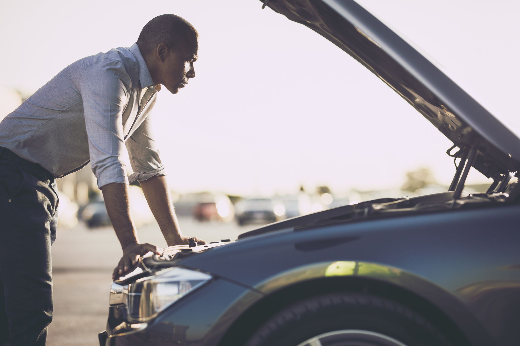 Mid adult black man analyzing his car after breakdown on the street.
