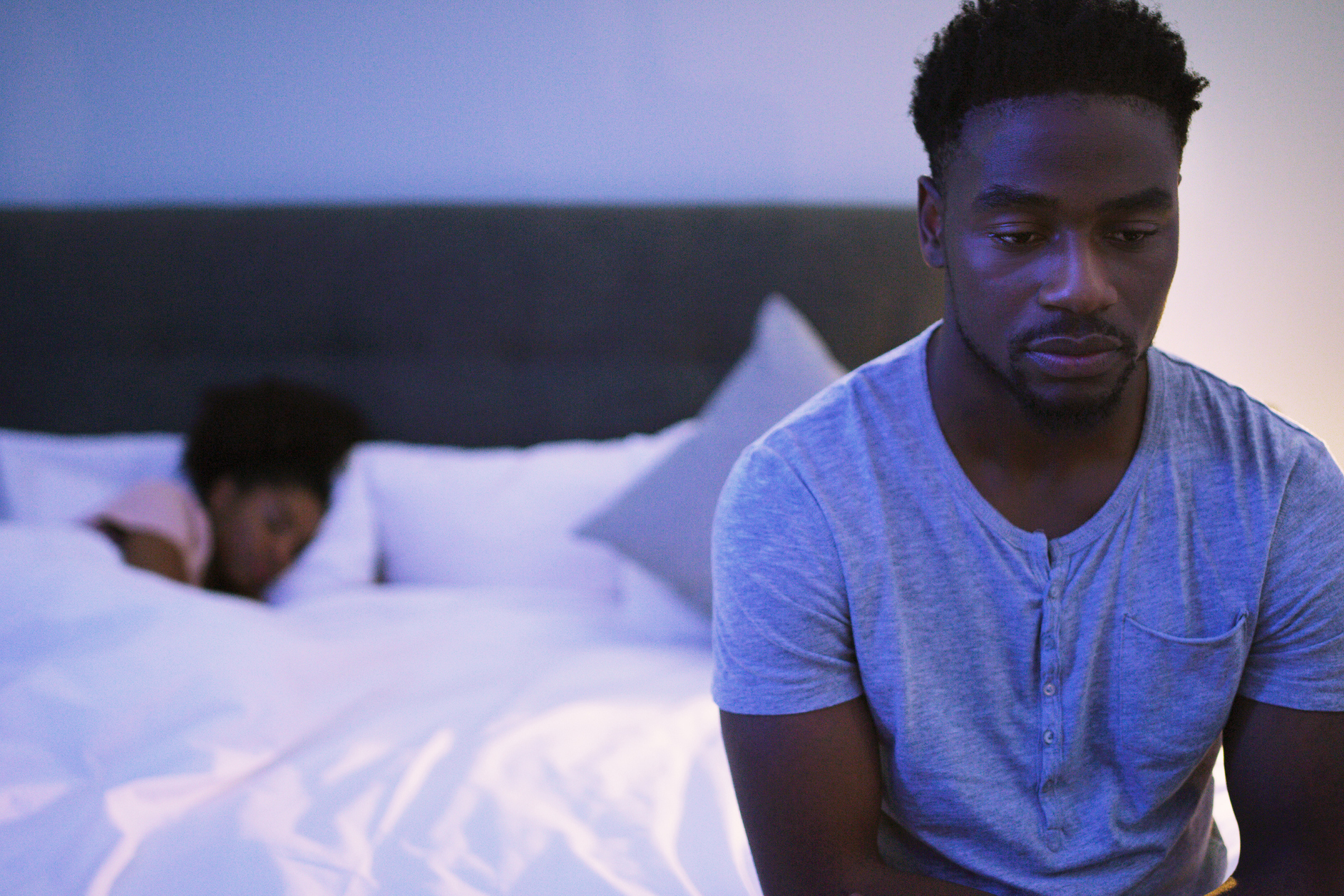 man sitting up in bed while woman sleeps
