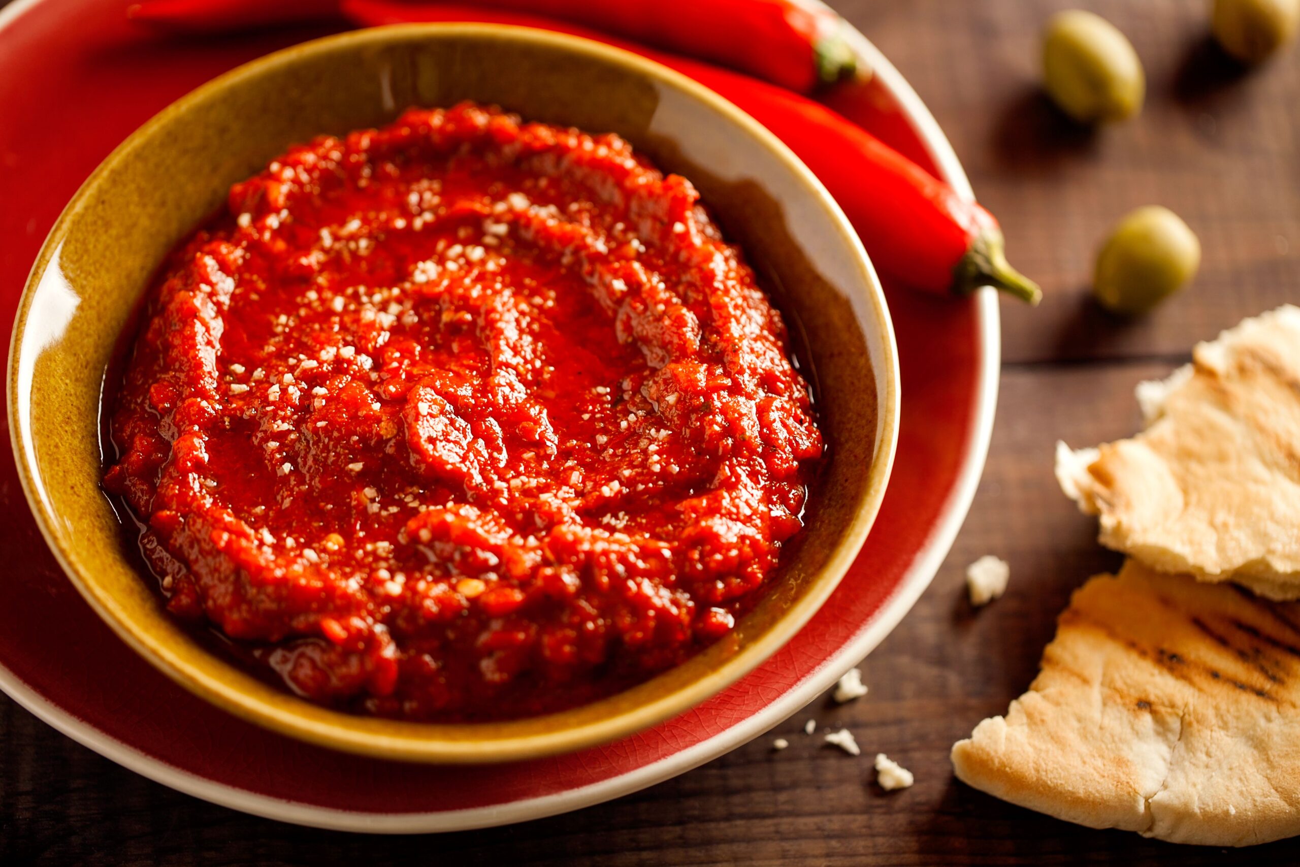 Healthy spicy, creamy vegetarian appetizer or snack with roasted red pepper dip with harissa, pita and olives close-up on wooden background. Traditional homemade Tunisia and Arabic cuisine adjika.