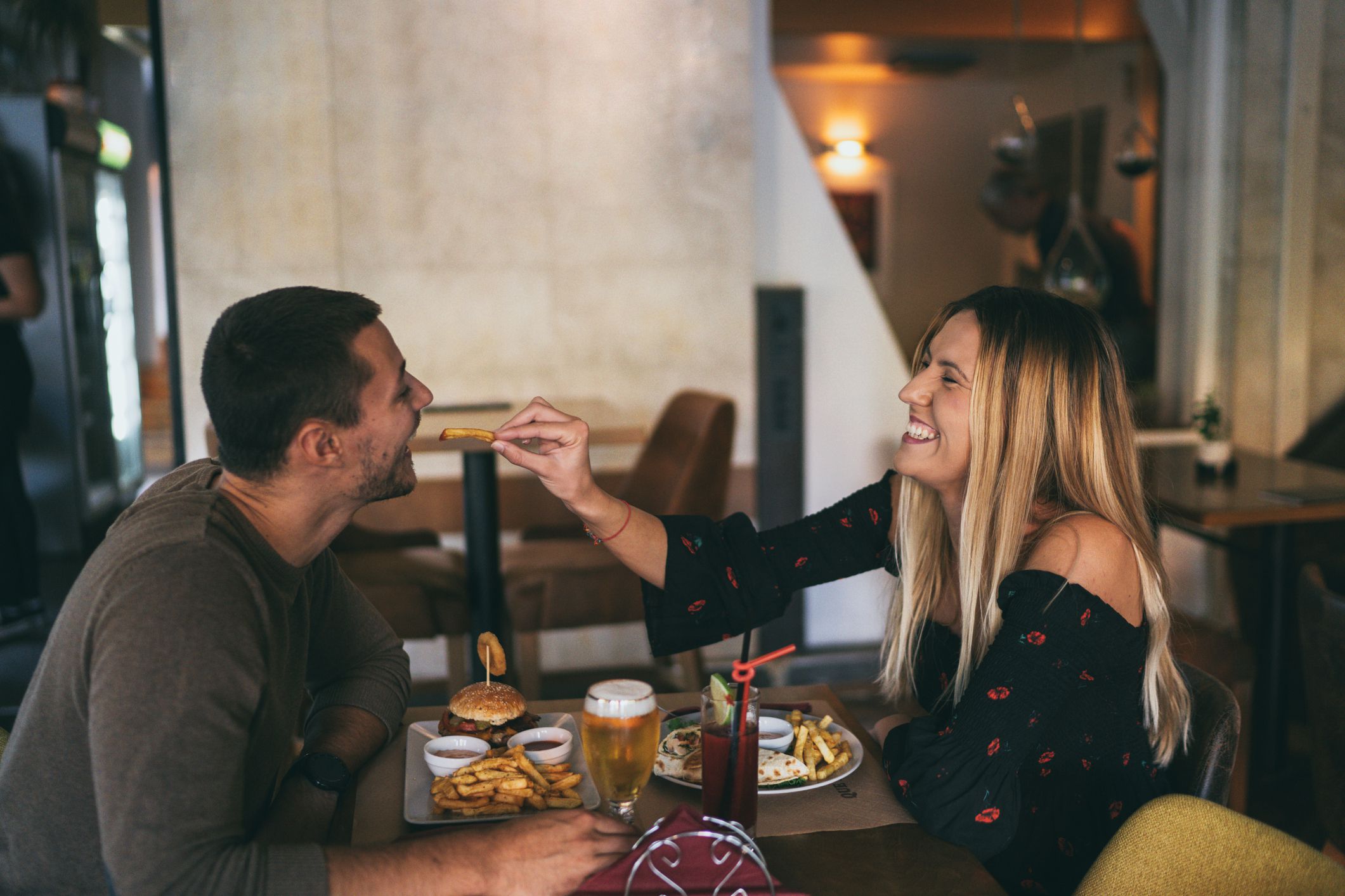 Loving young couple at restaurant, enjoying lunch together and sharing food, women feeds boyfriend with french fries