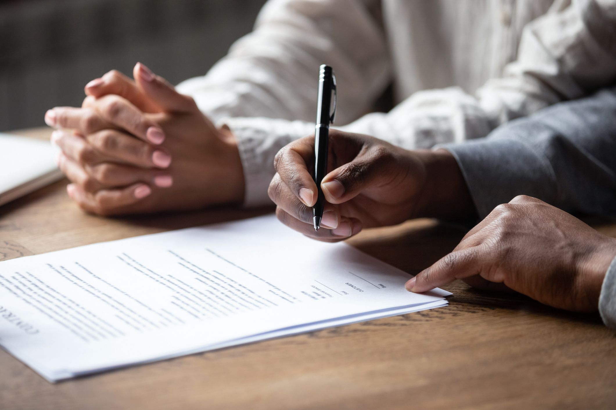 Close up of african American husband put signature on contract buying first house with wife, multiracial couple sign agreement closing deal with realtor or banker, taking property loan or mortgage