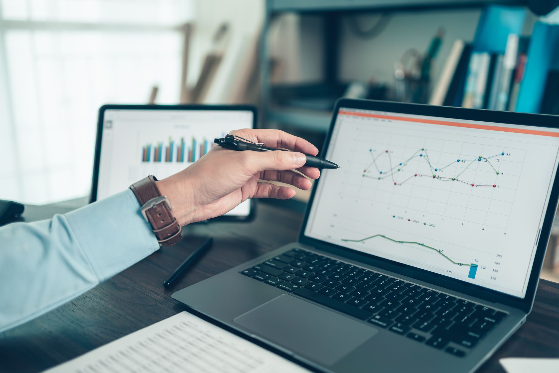 Business man hold stylus pen and pointing to laptop at office with document report, graph, financial report on screen.